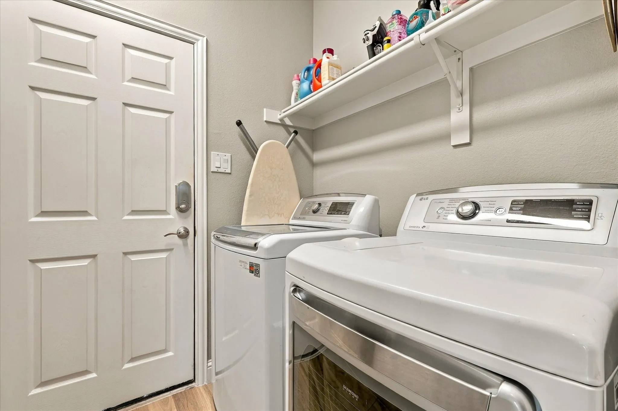 Laundry area featuring a white six-panel door, built-in upper shelving, and wood-finish flooring