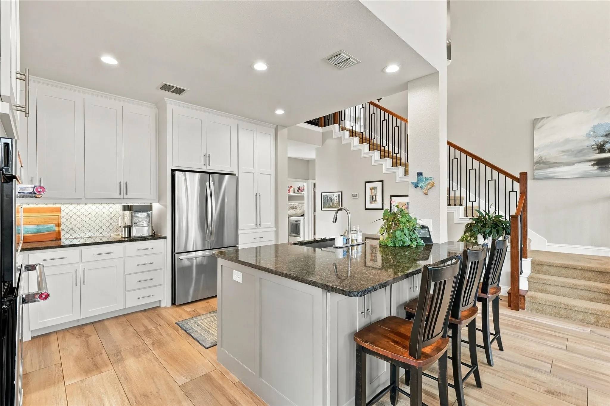 Kitchen featuring white cabinetry, stone countertops, stainless steel appliances, a center island with a sink, and wood-finish flooring