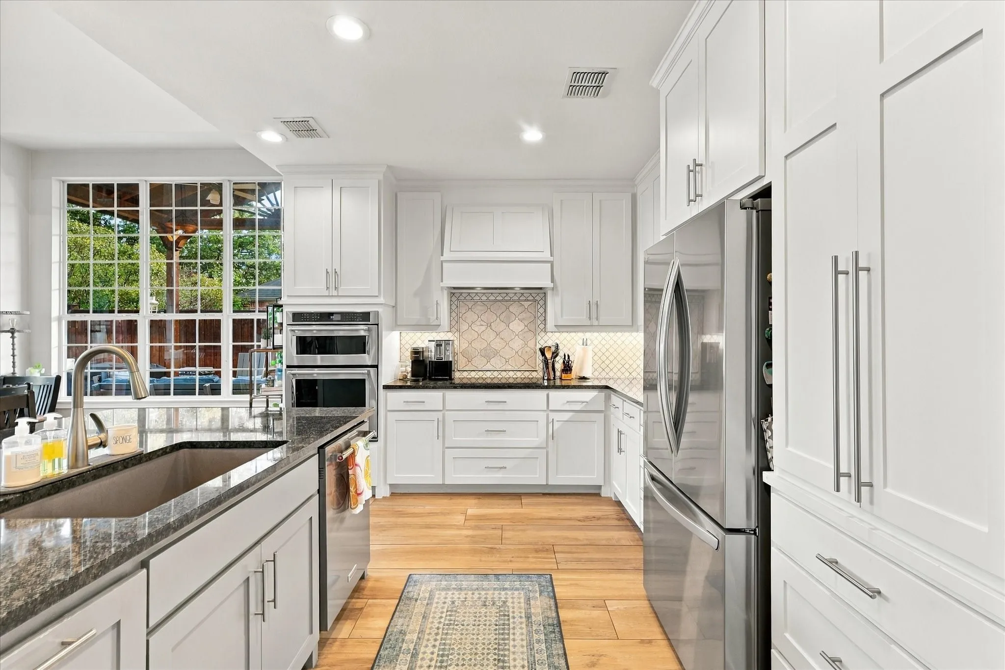 Kitchen featuring white cabinetry, wood-finish flooring, dark stone countertops, stainless steel appliances, and a tiled backsplash