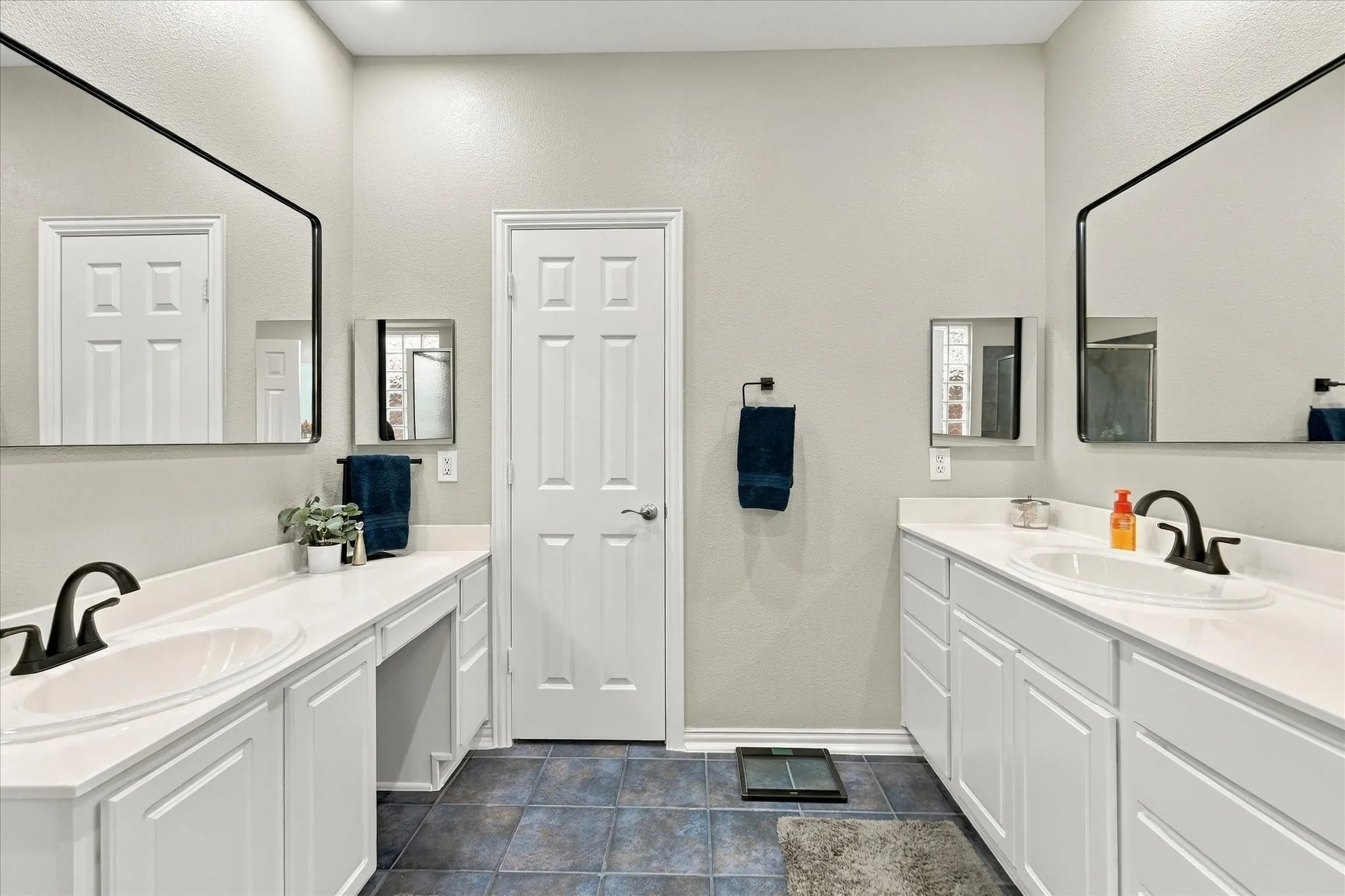 Dual vanity featuring white cabinetry, solid-surface countertops, integrated porcelain sinks, matte black fixtures, and expansive wall-mounted mirrors