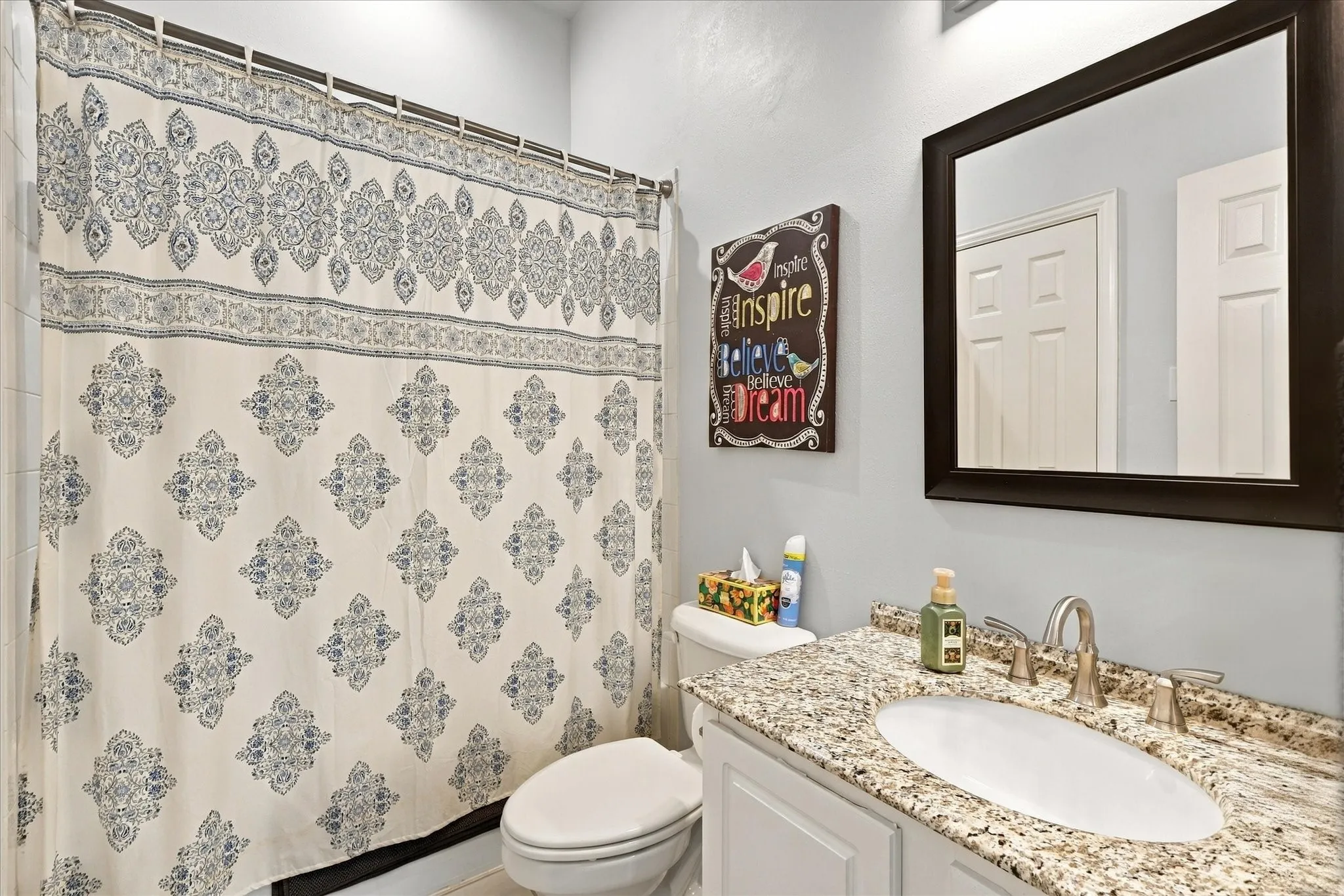 Bathroom featuring a stone-look countertop with an integrated oval basin, brushed nickel widespread faucet, white cabinetry, and a dark-toned framed mirror