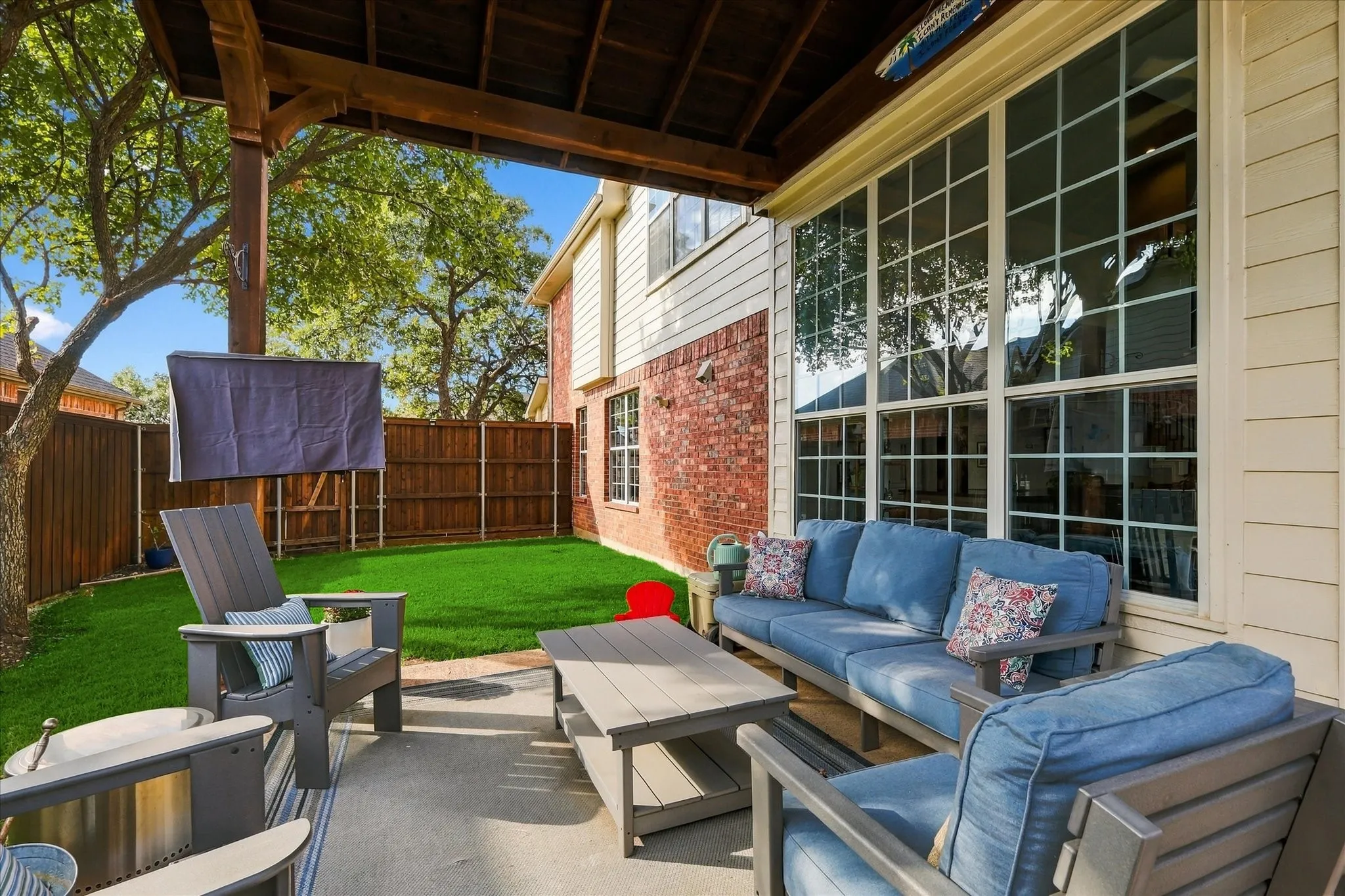 Covered patio featuring a concrete floor and wood-paneled ceiling, exterior brick and siding, multi-pane windows, and a fenced backyard with artificial turf