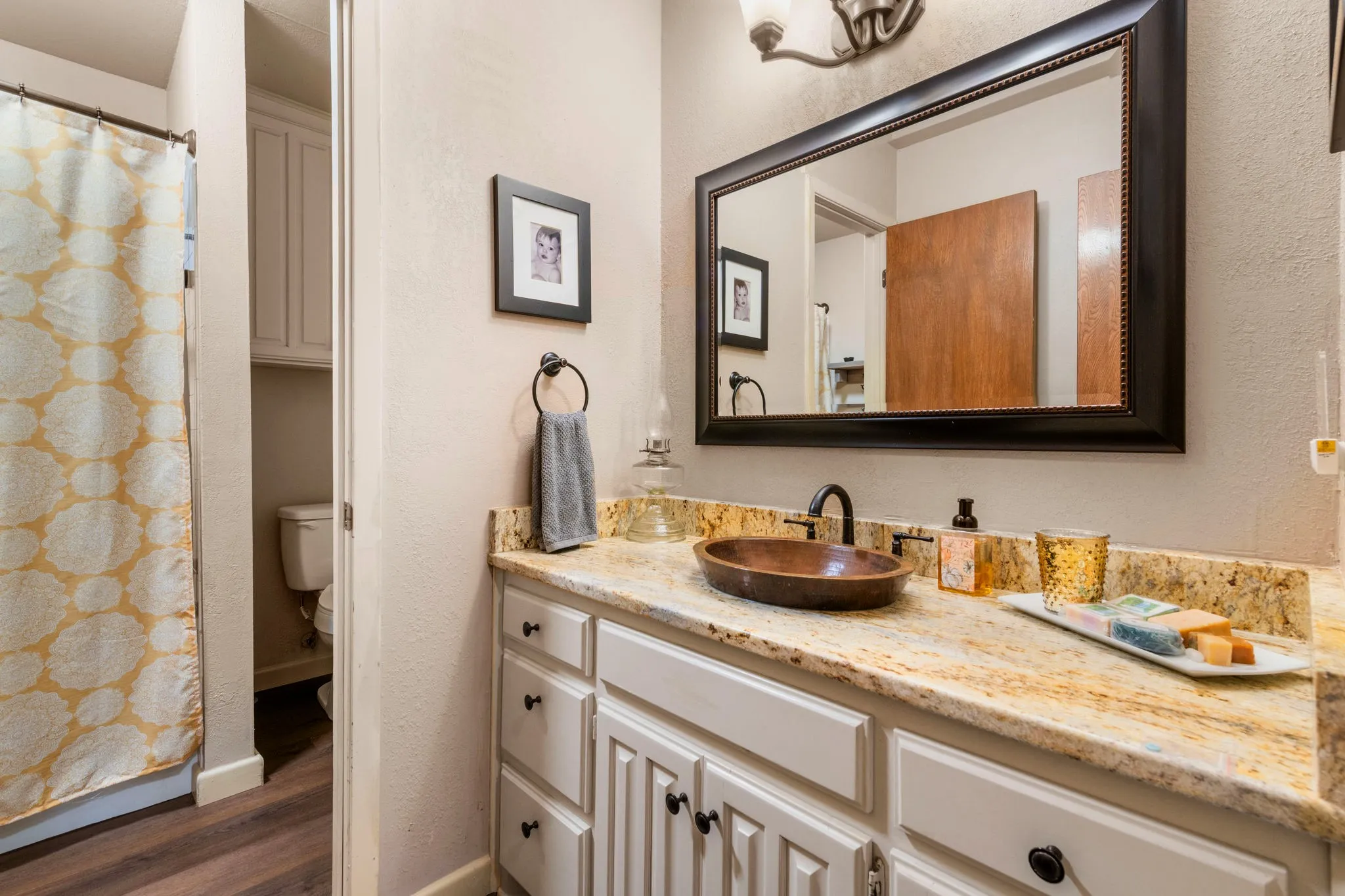 A hammered-copper basin gleams on golden-veined stone beside an oil-rubbed bronze faucet, giving the hall bath rustic-chic flair.