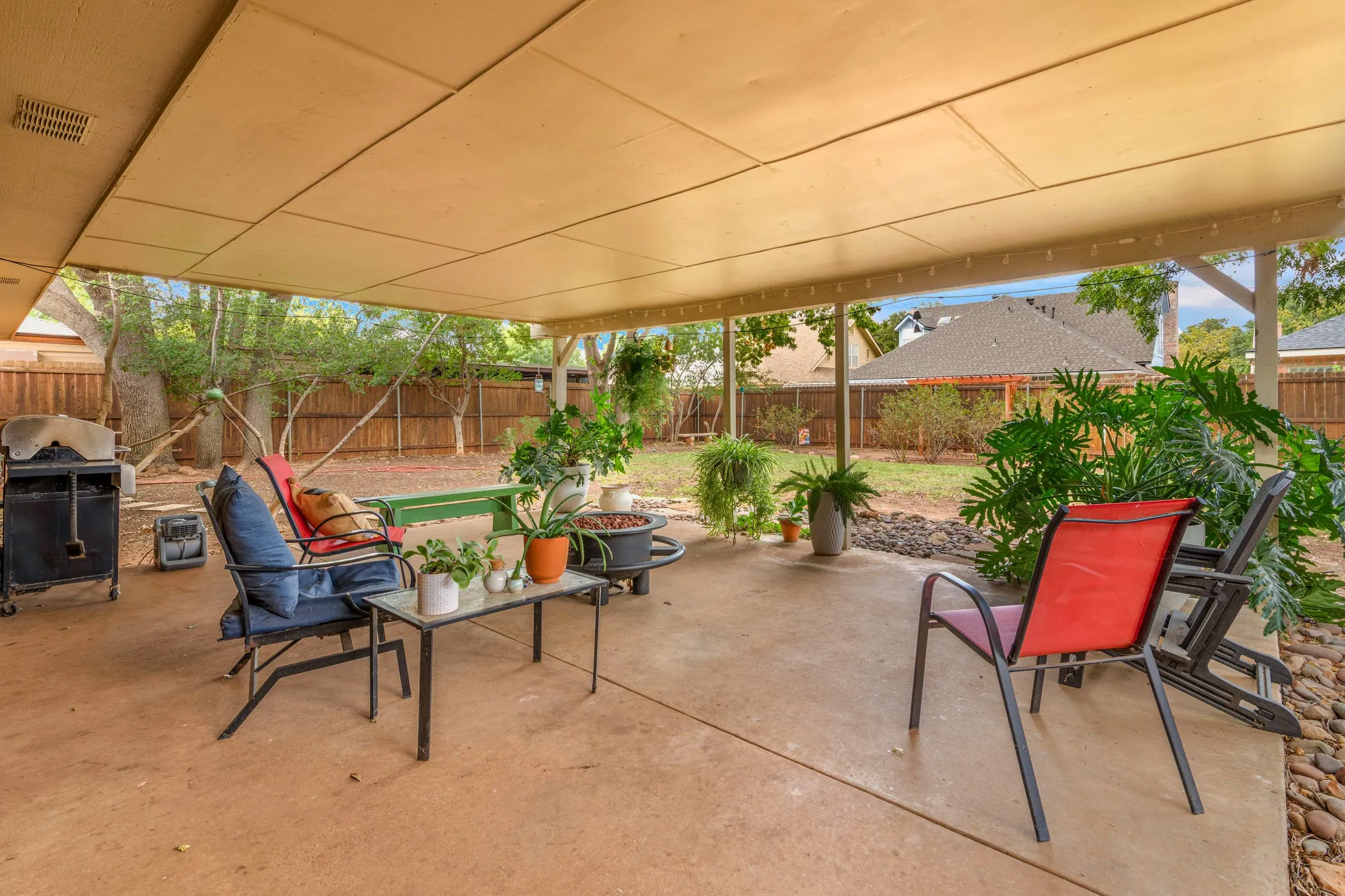 Tall 7' privacy fencing, a stretch of green grass, and a canopy of mature trees wrap this outdoor living space in seclusion, ready for gatherings from sunrise to starlight.