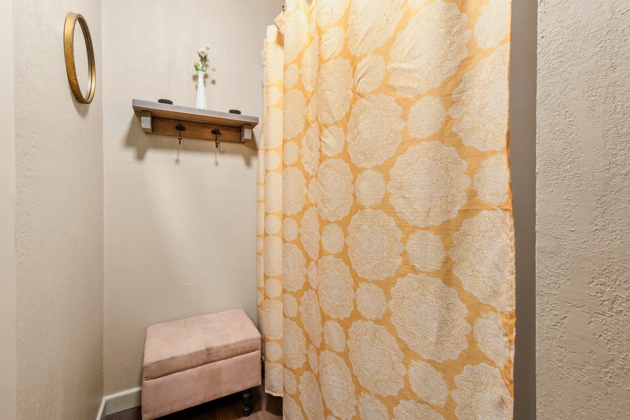 A gilded round mirror, a barn-wood hook shelf, and a blush ottoman beside a saffron mandala curtain make a charming dressing nook