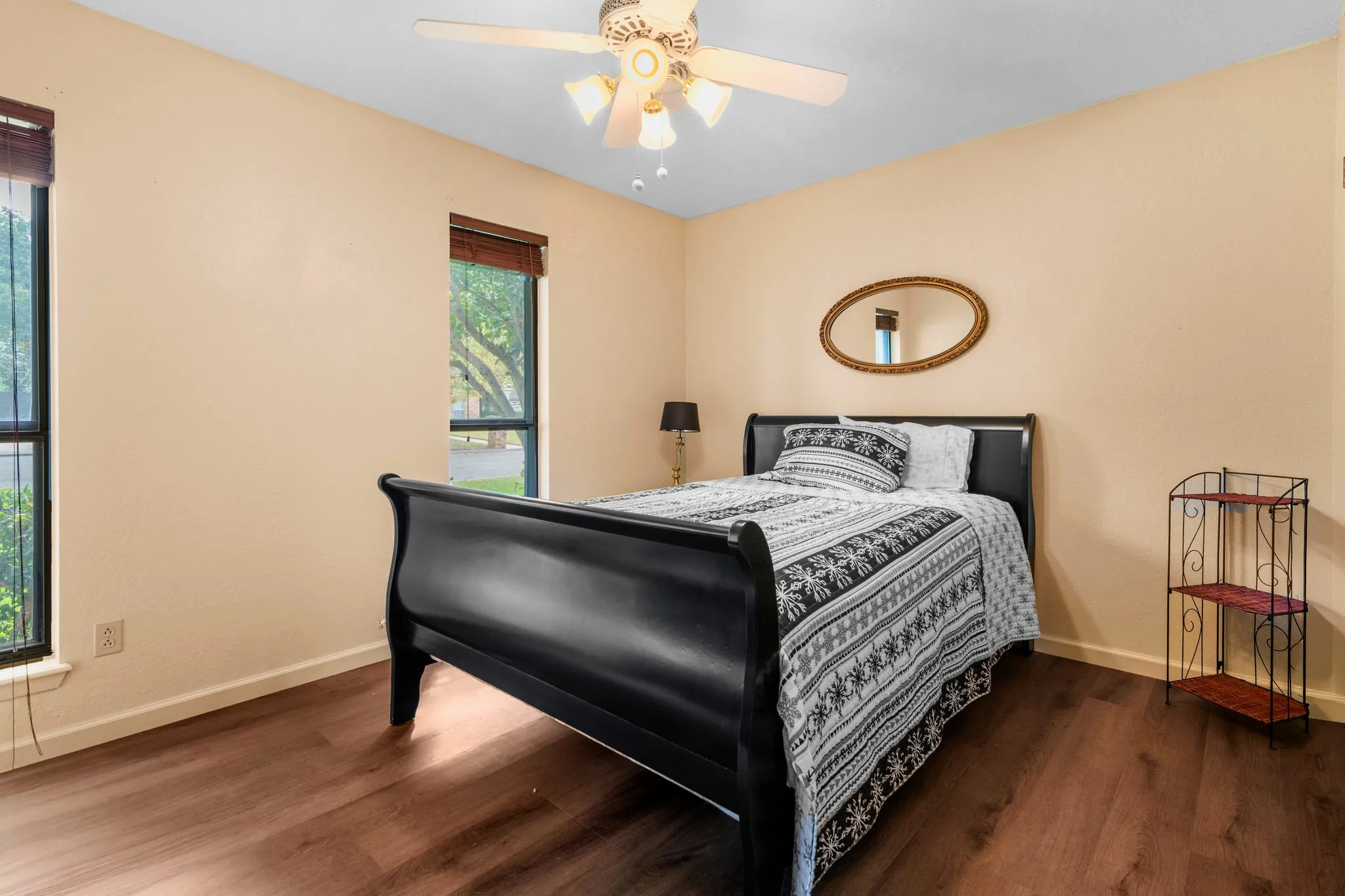 Honeyed paint, and leafy window views create a serene guest retreat beneath a five-blade ceiling fan.
