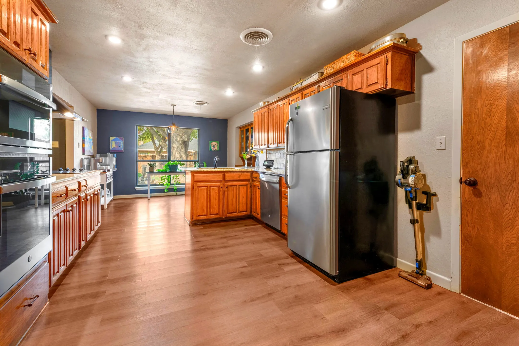 Warm wood cabinetry, stainless appliances, and a deep blue accent wall make this spacious kitchen timeless and welcoming.