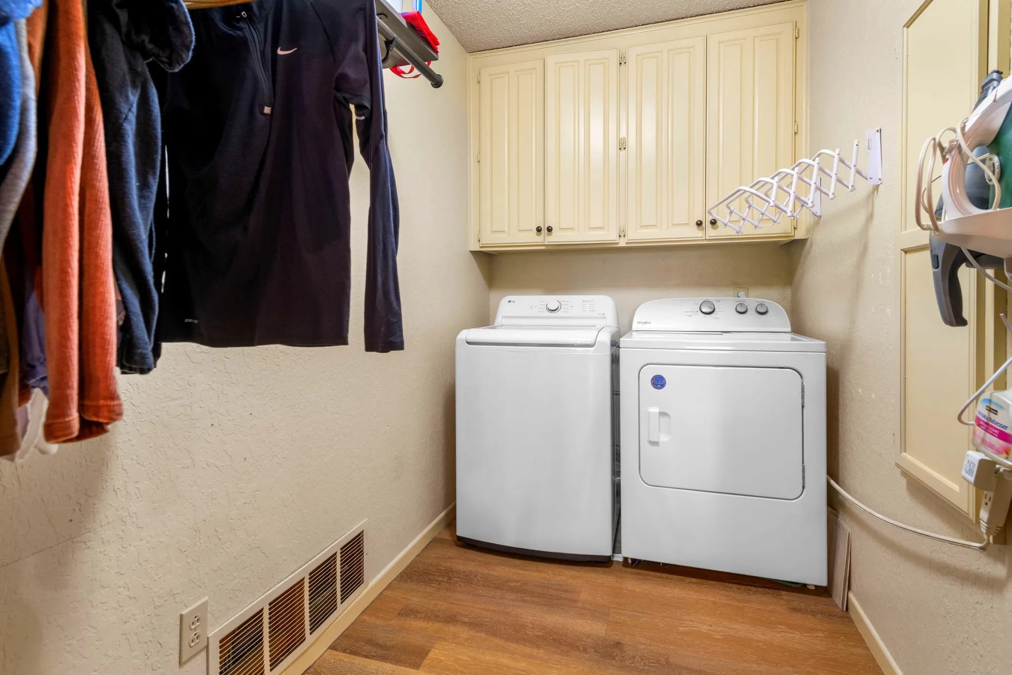A convenient laundry room with cabinet storage, a drying rack, and fresh new flooring.