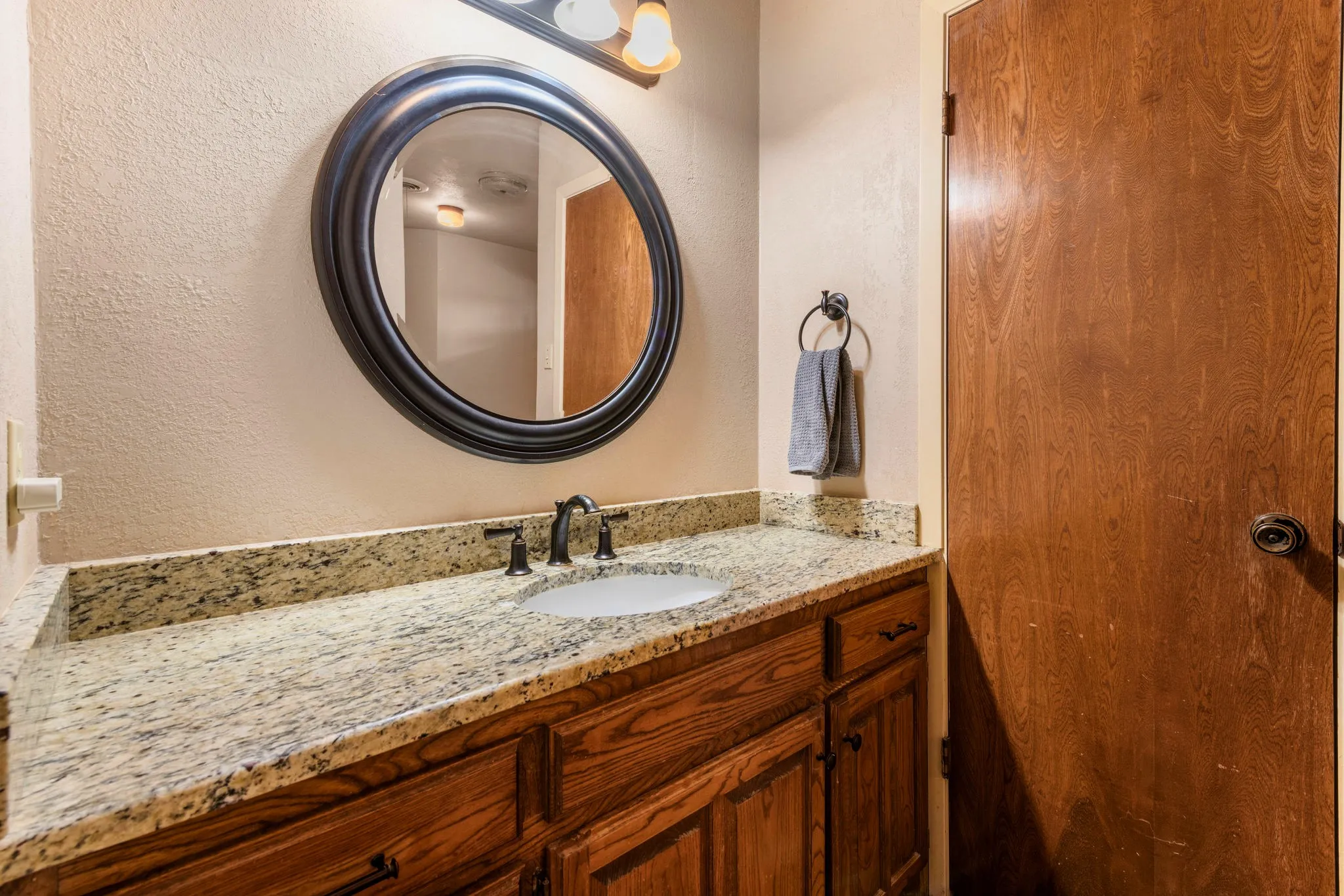 Honey-hued globe lights, a satiny white basin, and a boldly grained door finish the suite on a polished, practical note
