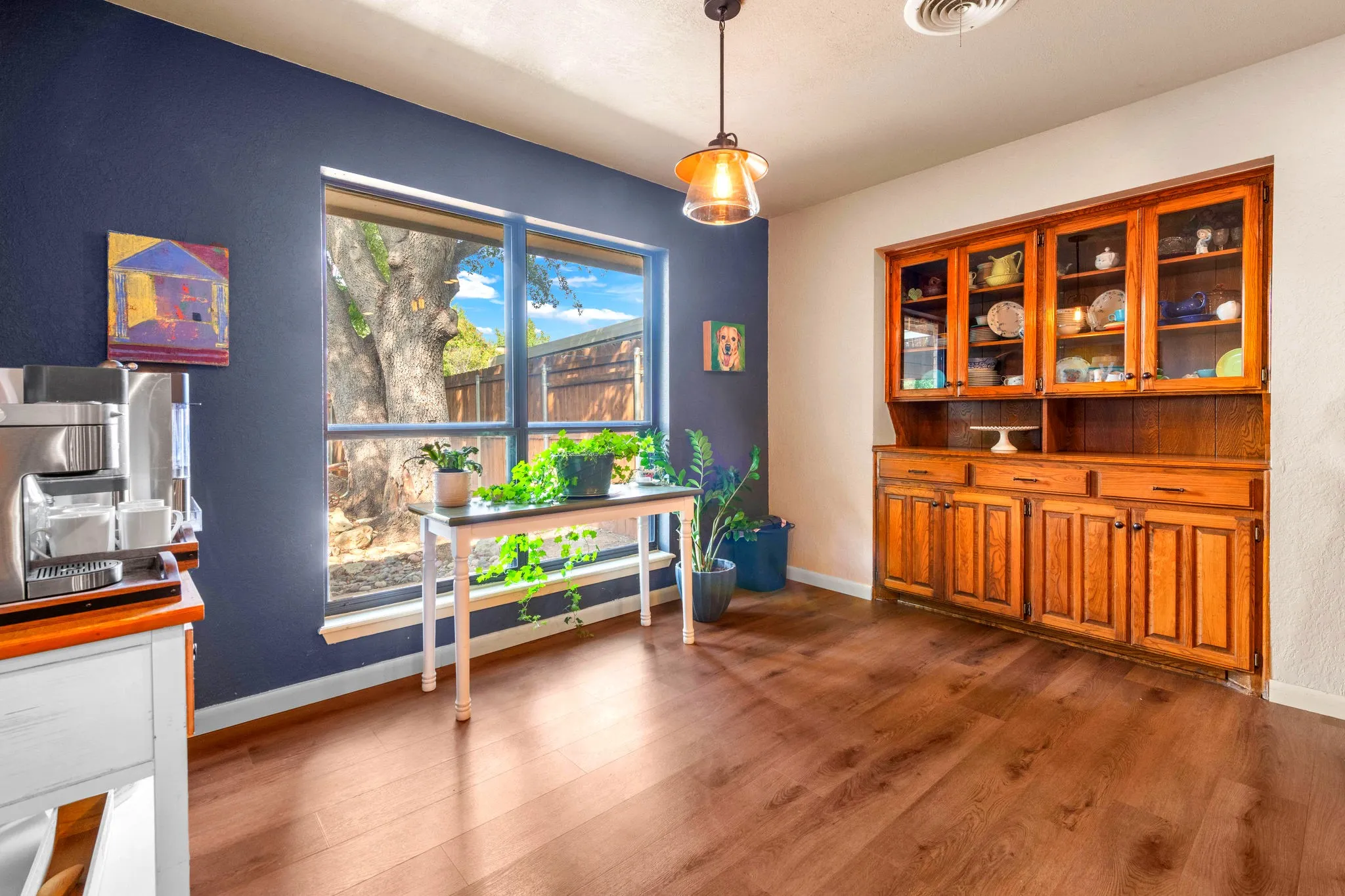 A deep blue accent wall and a large picture window with views of a mature oak make this dining nook a bright spot. A built-in glass-front cabinet adds storage and display space.