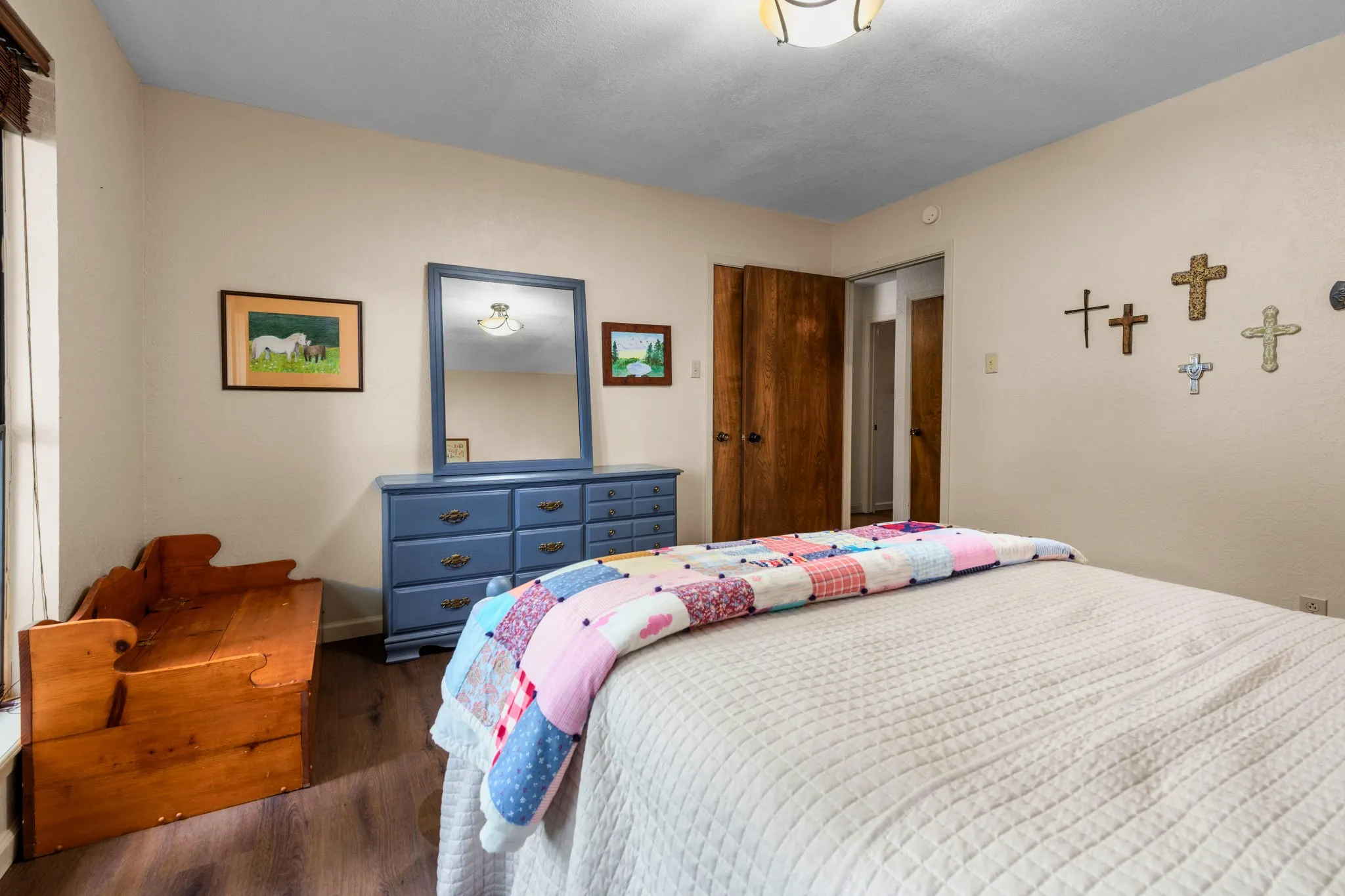Rich-toned floors ground this peaceful bedroom, where a sunlit side window, wood-paneled doors concealing storage, and a quiet hallway just outside make everyday living easy.