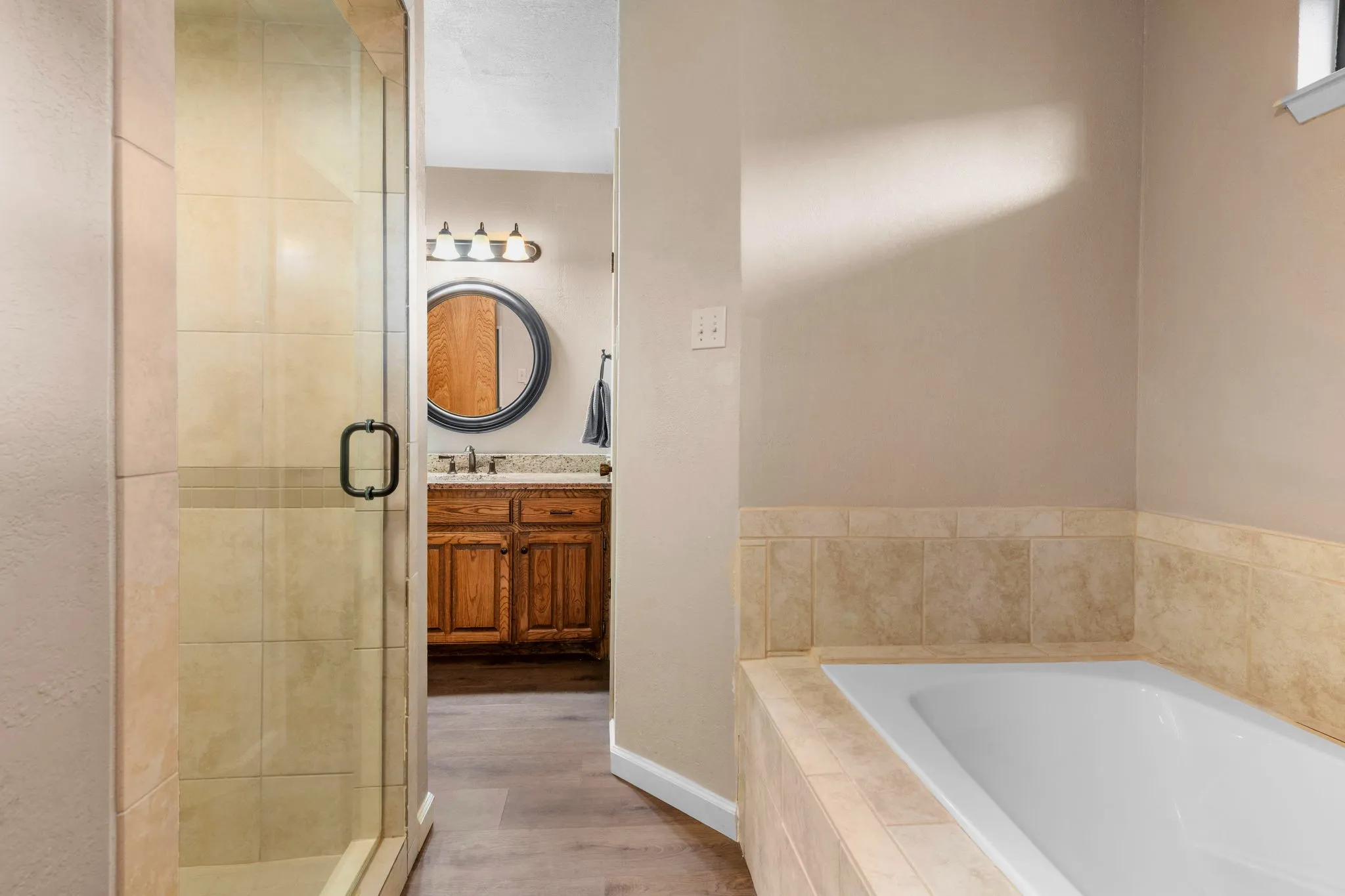 A glass-enclosed shower tiled in soft cream sits just beside the bathing area, with the vanity within easy reach.