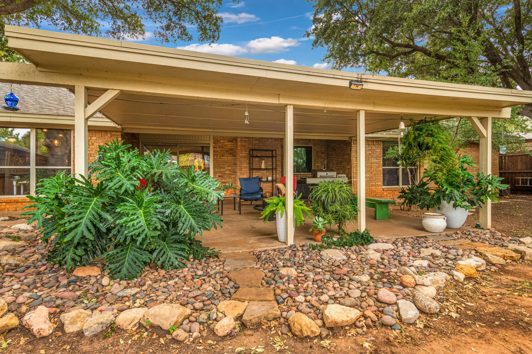 Lush, sculptural foliage rises from a river-rock garden, while flagstone steppers lead to a shaded lounging area and its handsome brick backdrop.