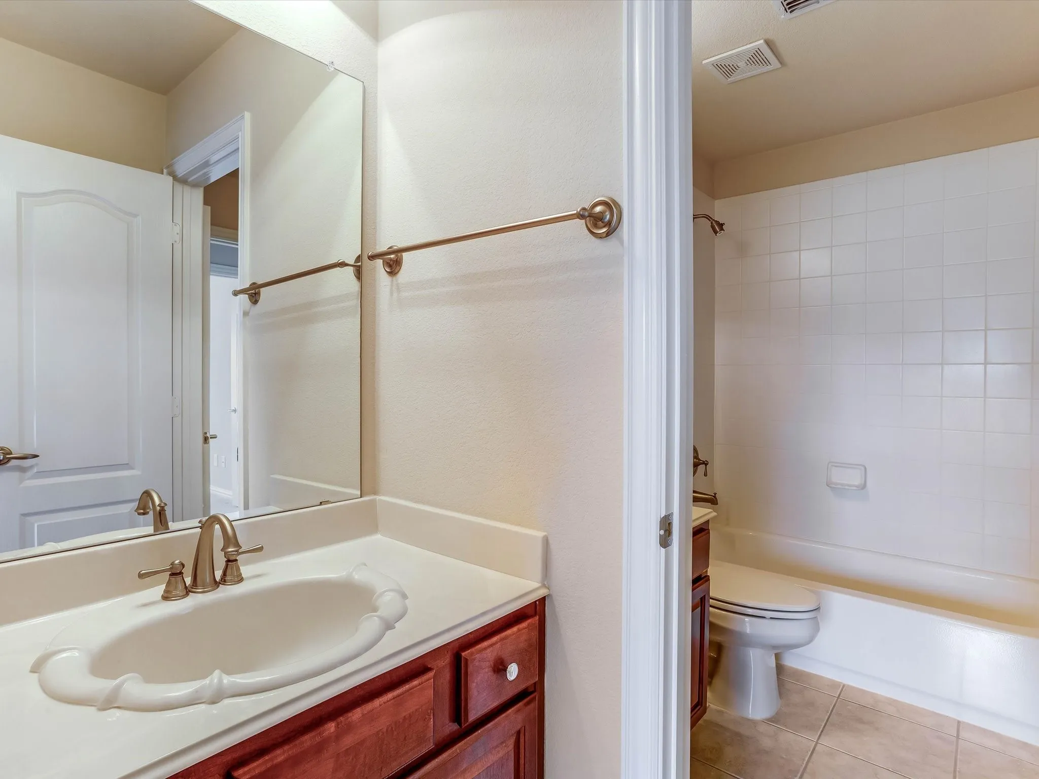 Bathroom featuring wood-finish cabinetry, a white countertop with an integrated basin, brass-tone hardware, a wall-mounted mirror, and a tiled tub-shower combination