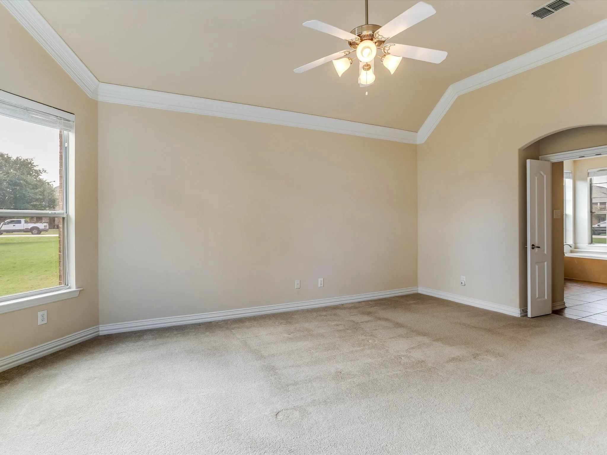 Vaulted ceiling featuring crown molding, neutral carpeting, a central ceiling fan with multi-light fixture, and an arched doorway entry