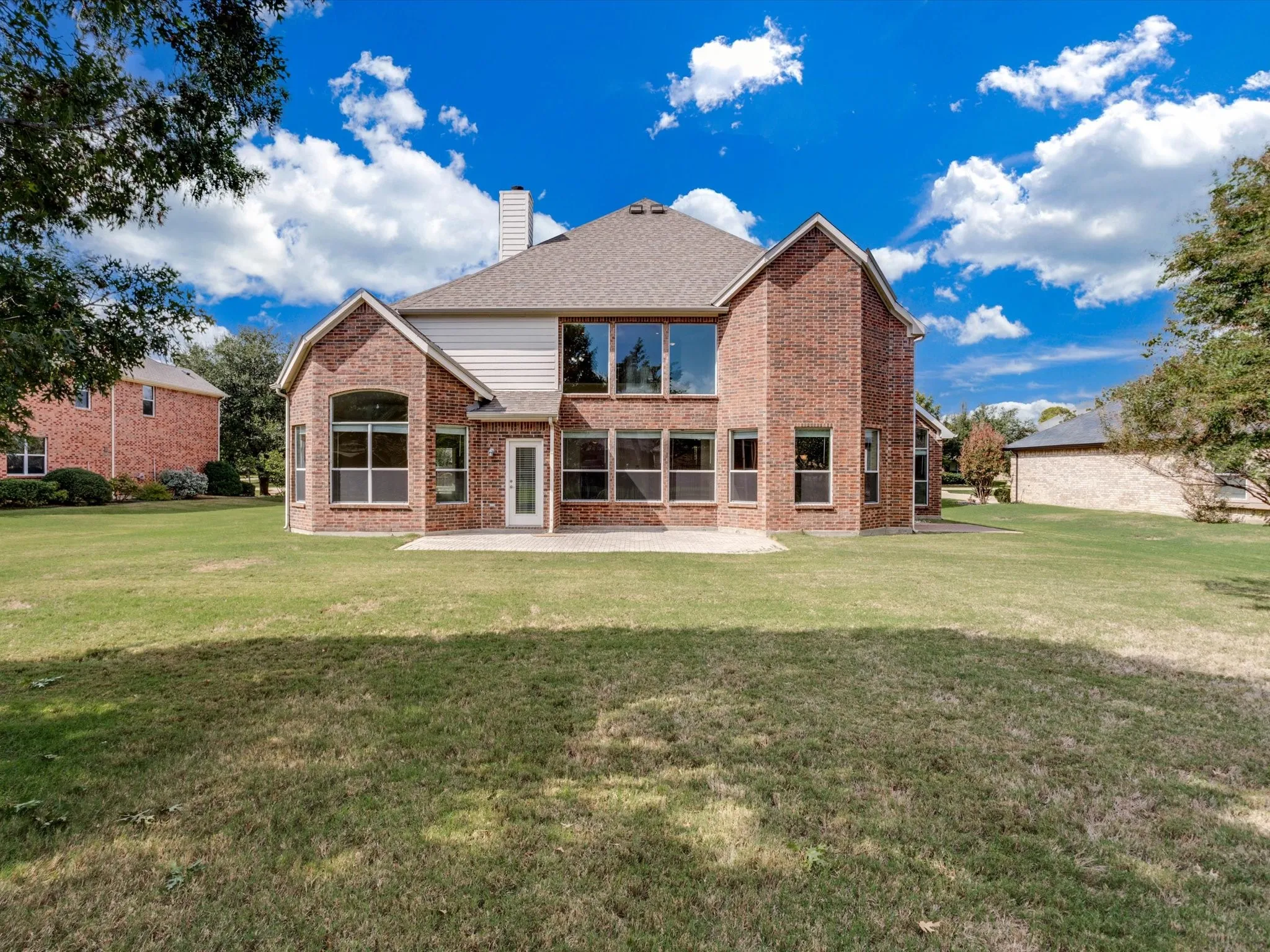 Multi-story brick exterior featuring a multi-gabled roofline, expansive rear lawn, and a concrete patio