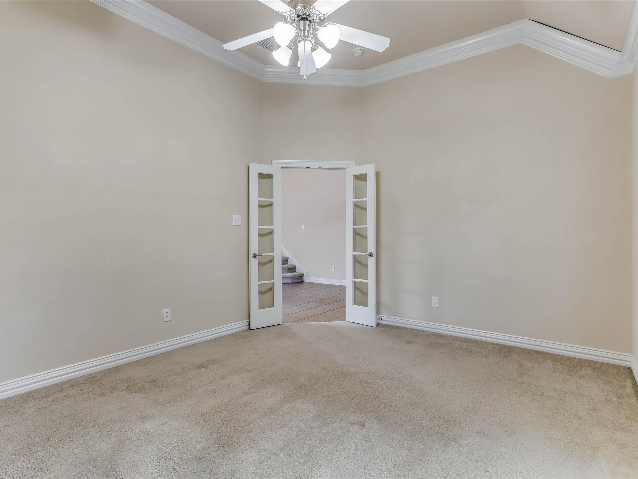 Vaulted ceilings featuring decorative crown molding, white French doors, and a central ceiling fan with multi-light fixture