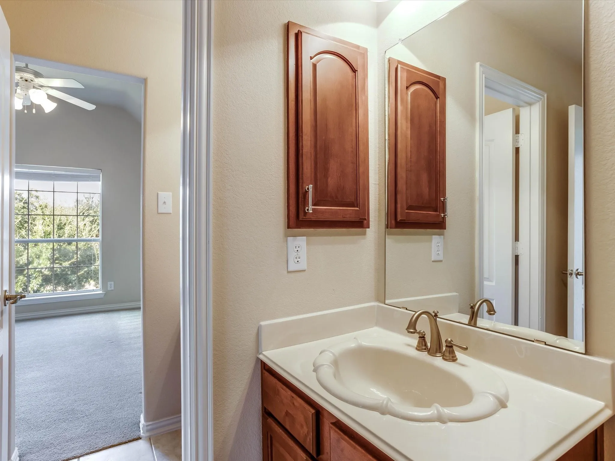 Bathroom featuring a vanity with wood-finish cabinetry, an integrated sink basin, a decorative high-back mirror, and brass-tone hardware