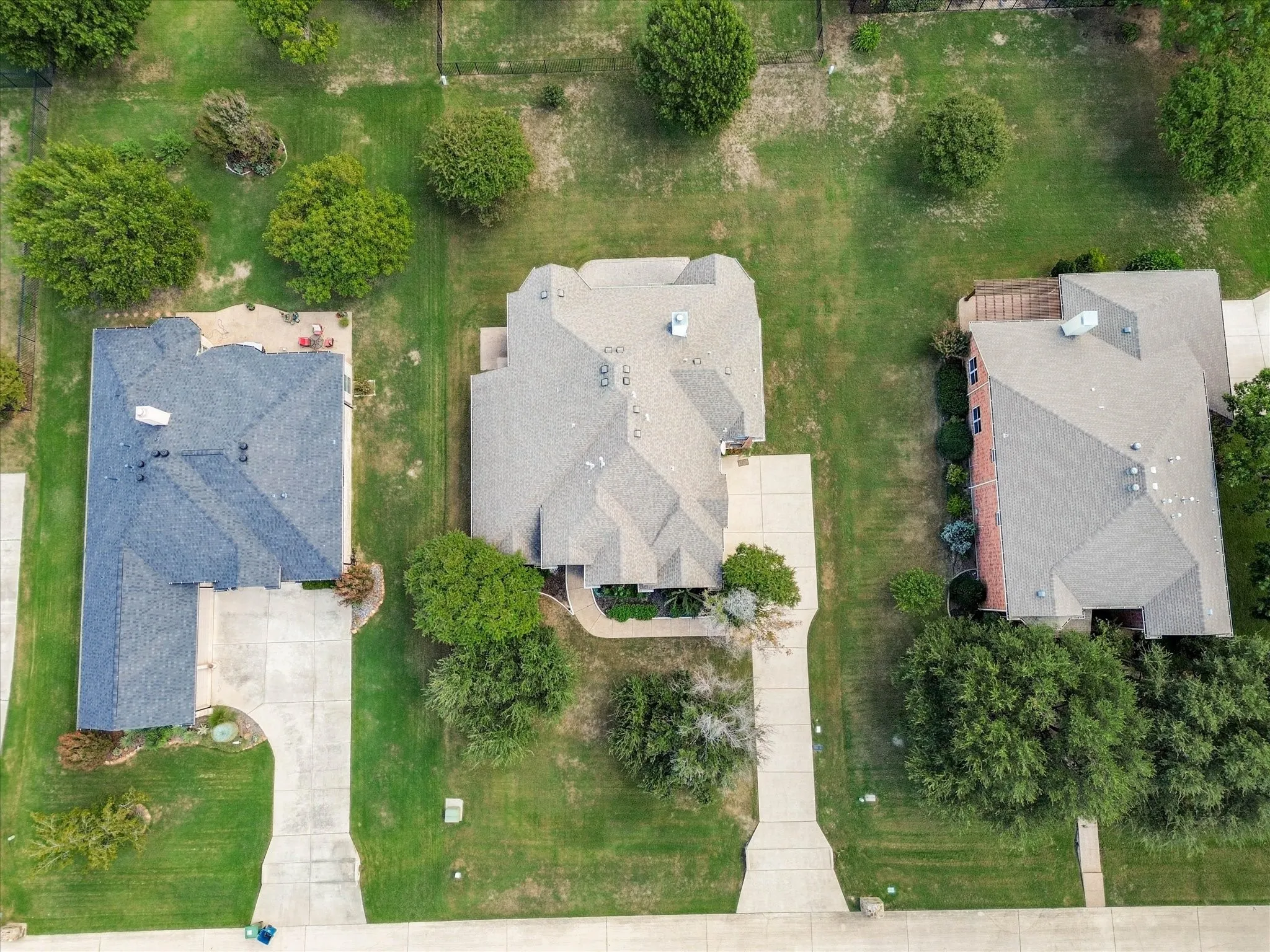 Aerial perspective featuring residential lots with concrete driveways, manicured lawns, and mature trees