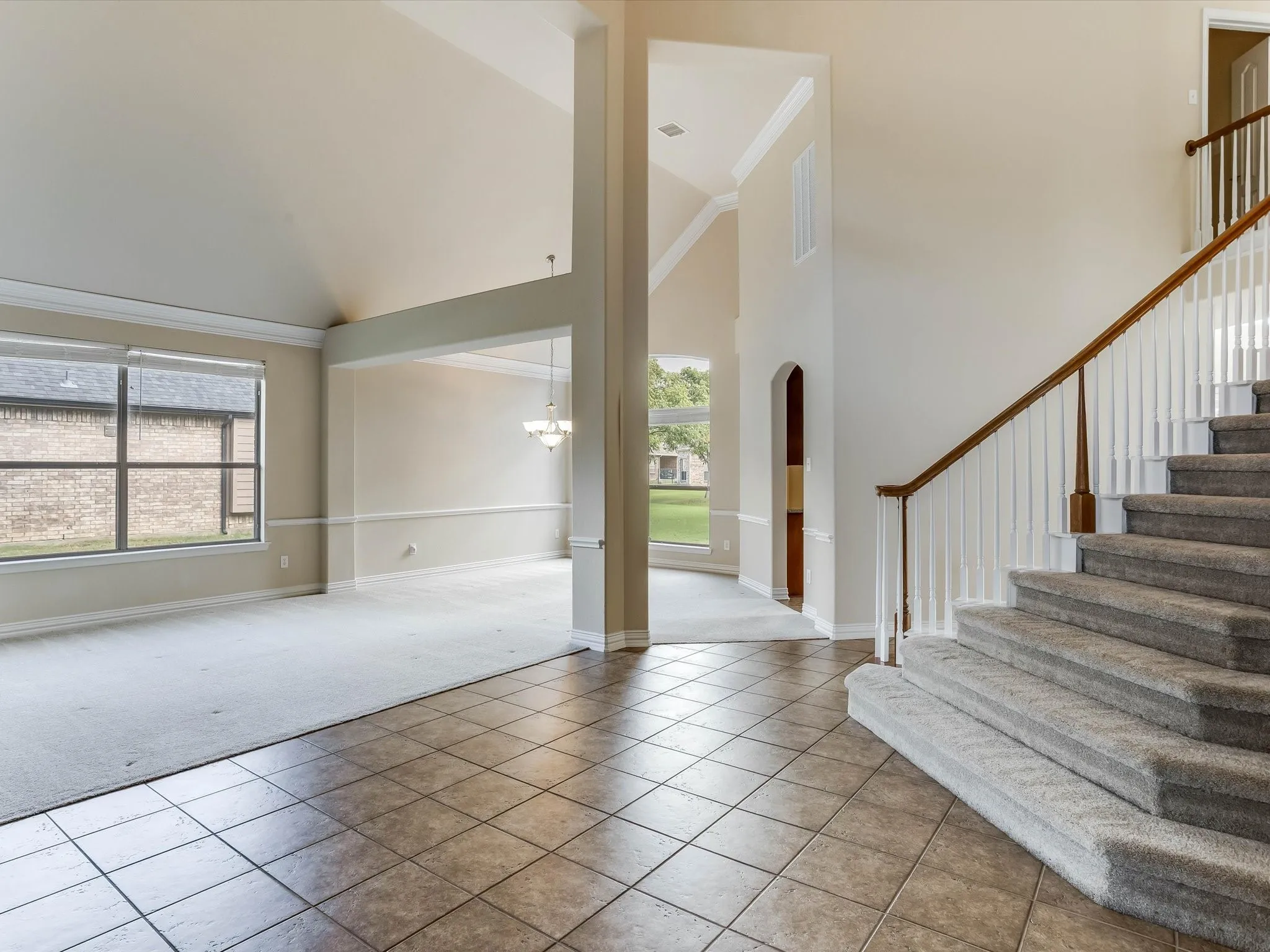 Vaulted ceilings with crown molding, ceramic tile flooring, staircase featuring a wood handrail with white balusters, and large windows
