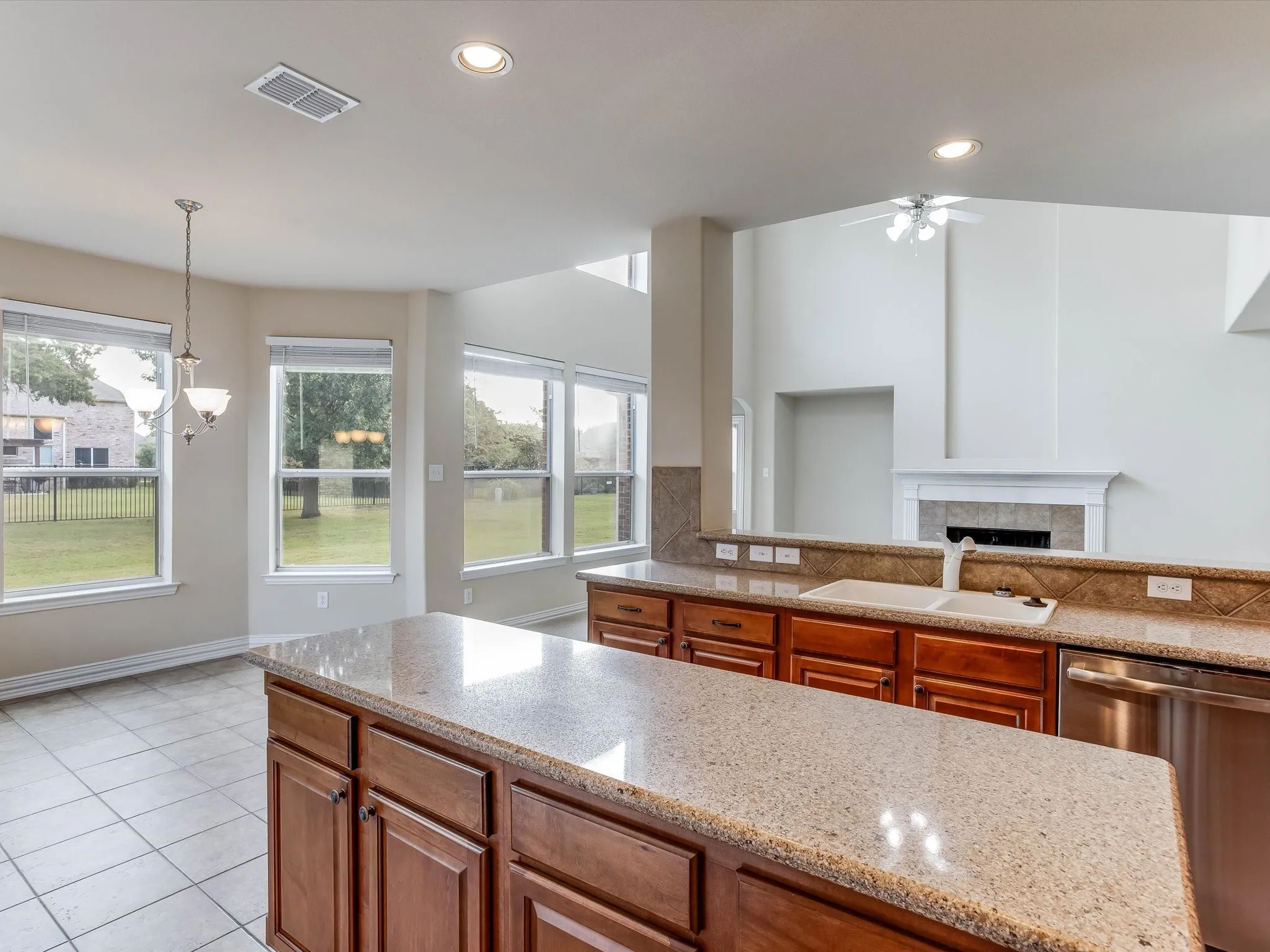 Kitchen featuring wood cabinetry, stone countertops, integrated double-basin sink, stainless steel dishwasher, and tile flooring