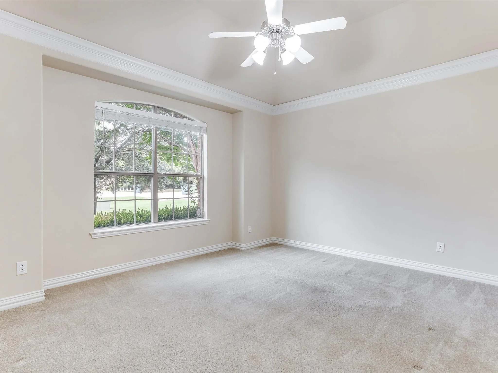 Tray ceiling with crown molding, arched window, and central ceiling fan
