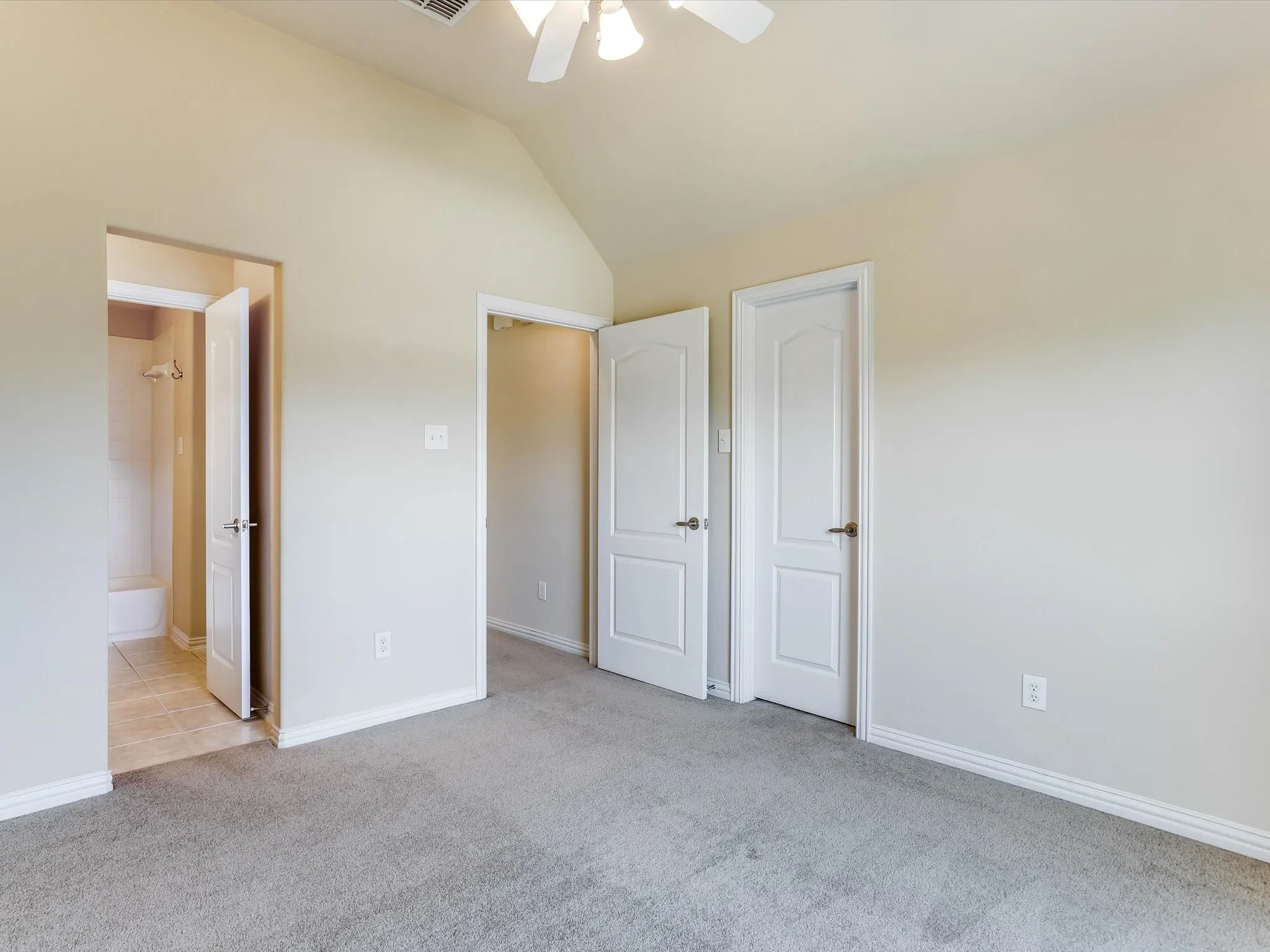 Vaulted ceiling featuring a central light fixture, neutral carpeted flooring, and white two-panel interior doors