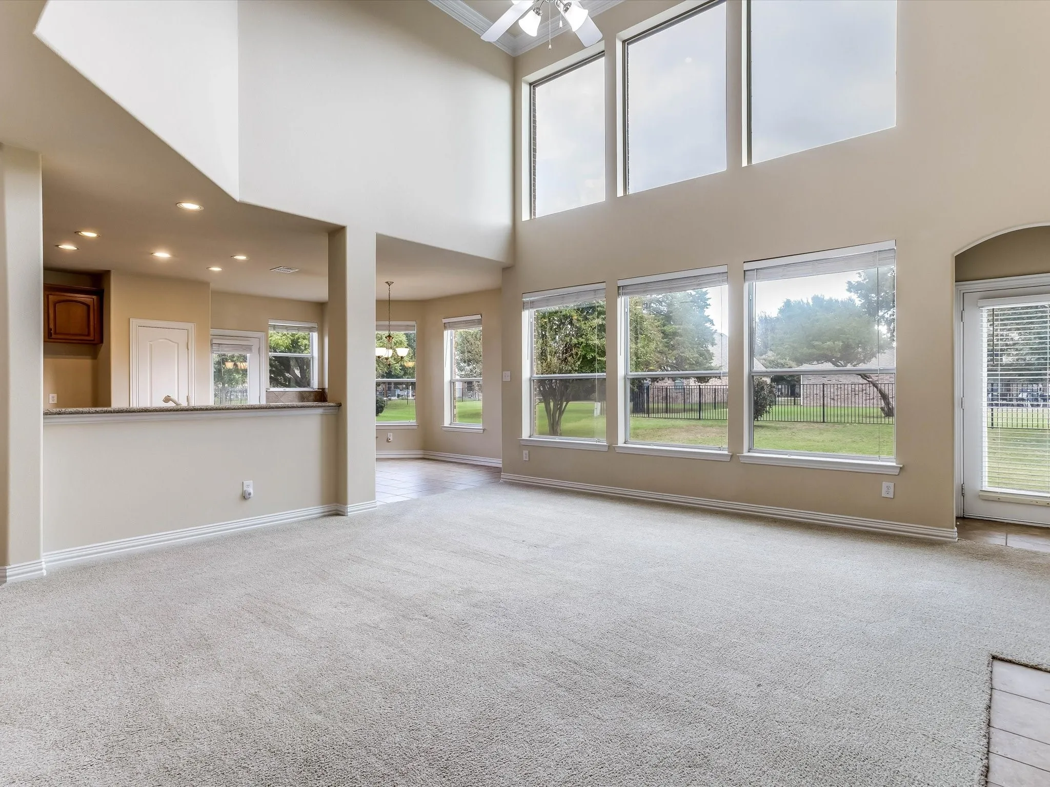 Double-height ceilings, expansive window wall, neutral carpeting, recessed lighting, and a kitchen pass-through counter