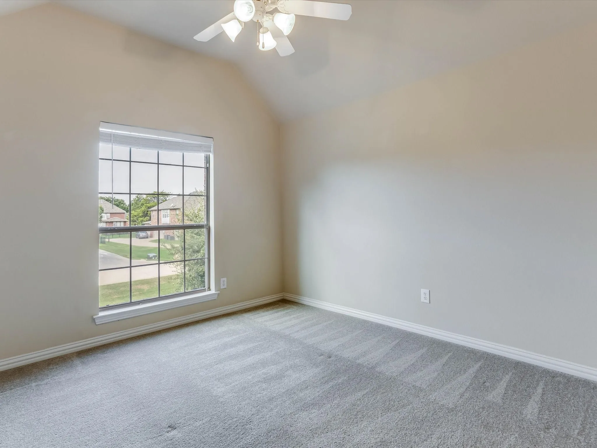 Vaulted ceiling featuring a central multi-light fan, large multi-pane window, and wall-to-wall carpeting