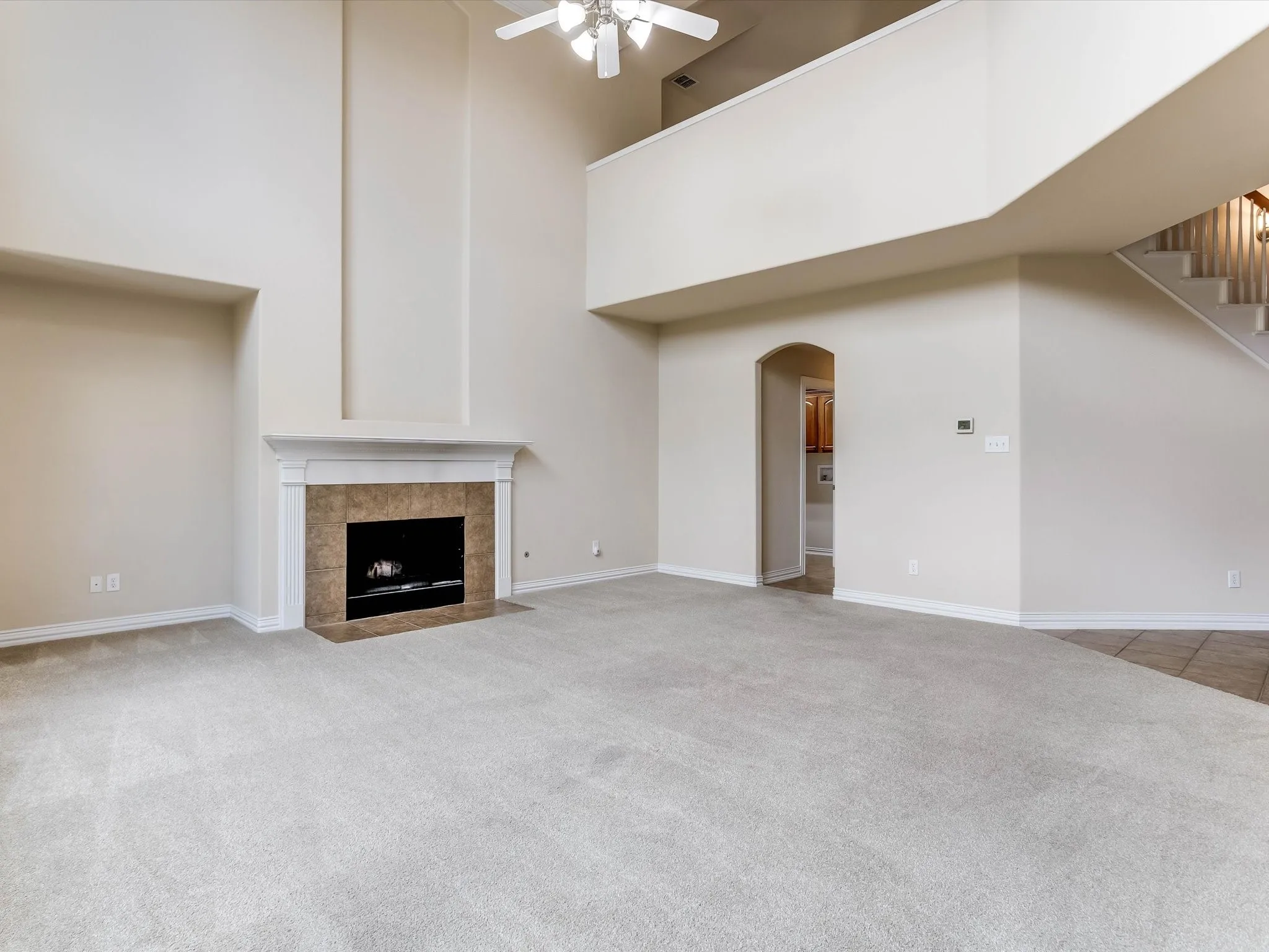 High-ceiling living area featuring a neutral color palette, a floor-to-ceiling architectural niche, a fireplace with a stone-tile surround and mantel, and an overlook with a staircase