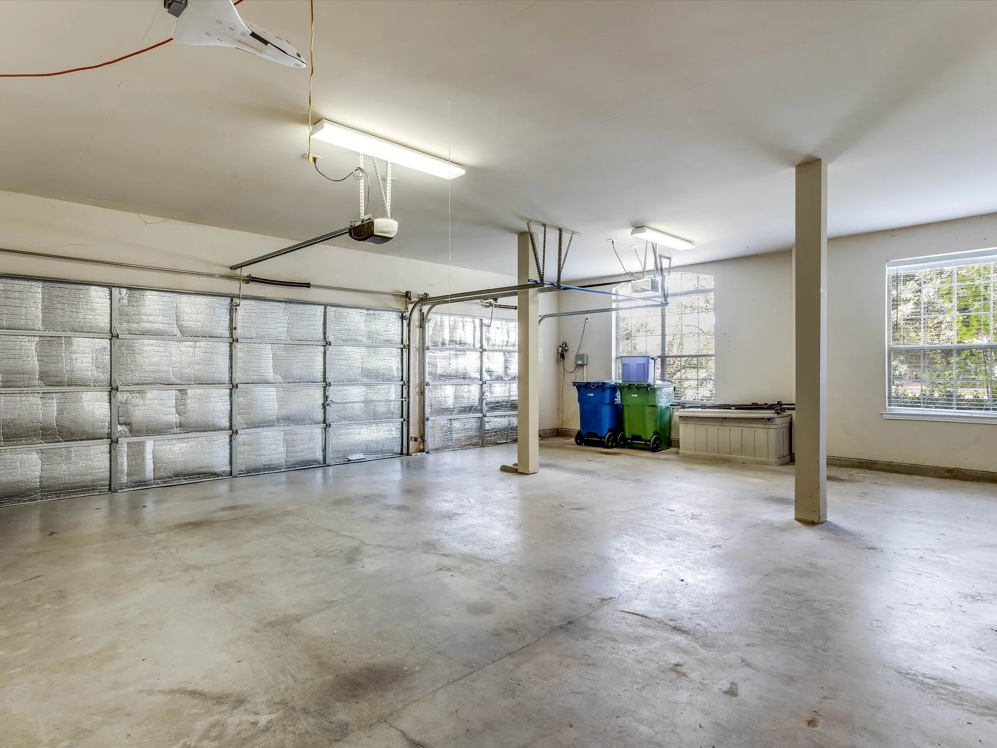 Multi-vehicle garage featuring insulated garage doors, concrete flooring, structural support columns, and dual-pane windows