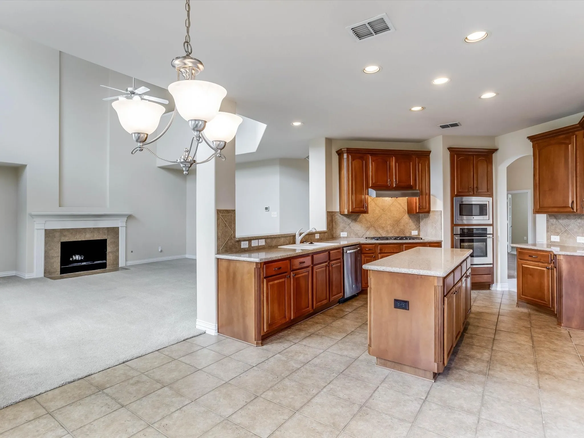 Kitchen featuring wood cabinetry, stone-finish countertops, tile backsplash, built-in wall oven, and a center island, complemented by a fireplace with stone surround