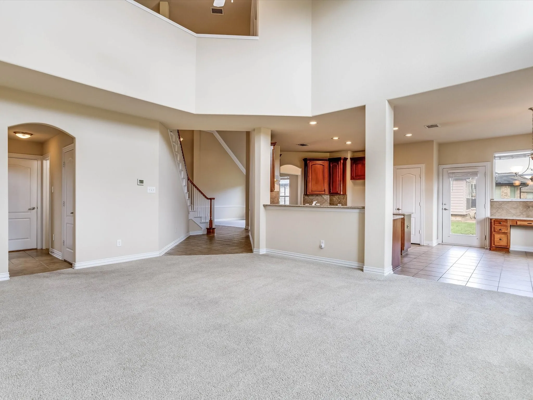 Expansive living area featuring vaulted ceilings, neutral carpeting, recessed lighting, a built-in kitchen peninsula, and a staircase with wood handrails