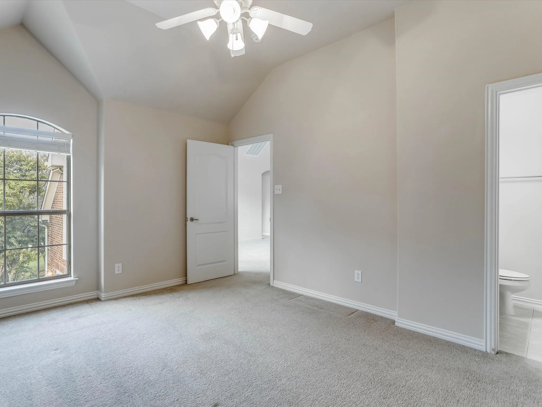 Vaulted ceilings, arched window with grid detail, neutral wall tones, carpeted flooring, and ceiling fan with integrated lighting