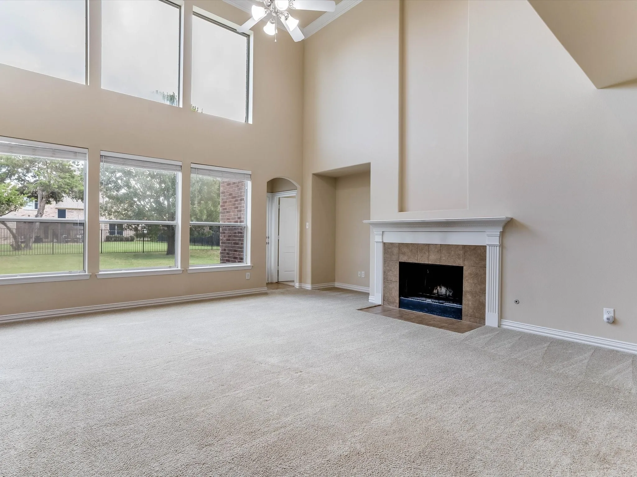 High-ceilinged room featuring expansive floor-to-ceiling windows, a fireplace with a white mantel and tile surround, and a ceiling-mounted light fixture