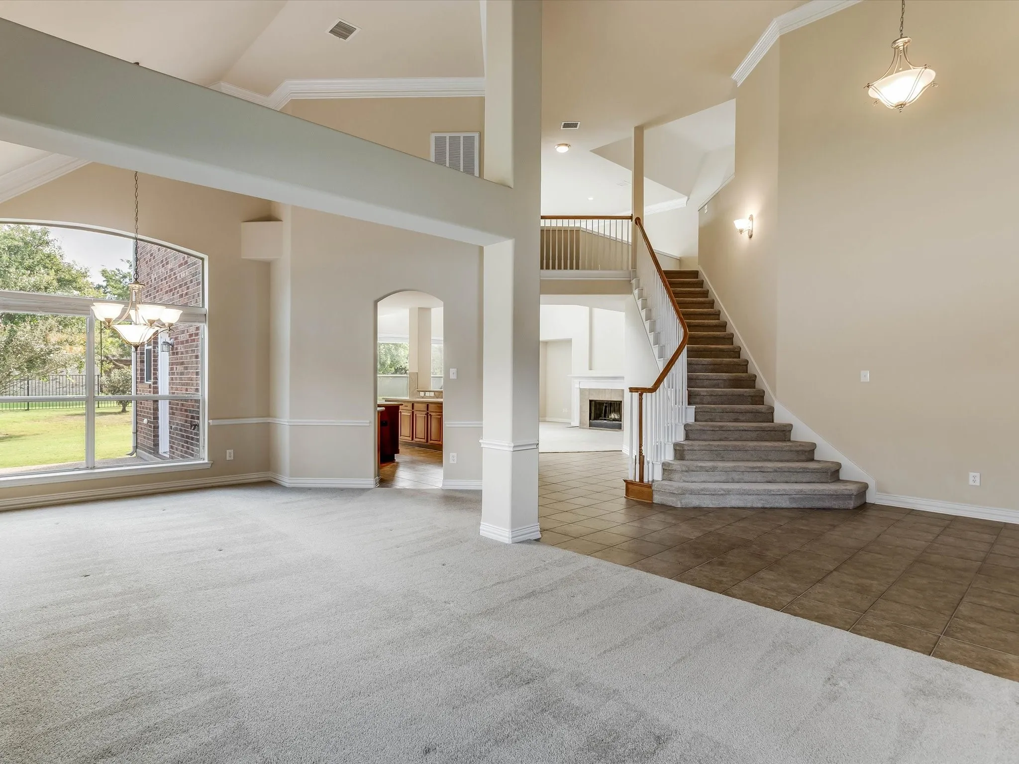 Vaulted ceilings, expansive arched windows, ceramic tile and carpeted flooring, a staircase with a wooden handrail, and built-in crown molding