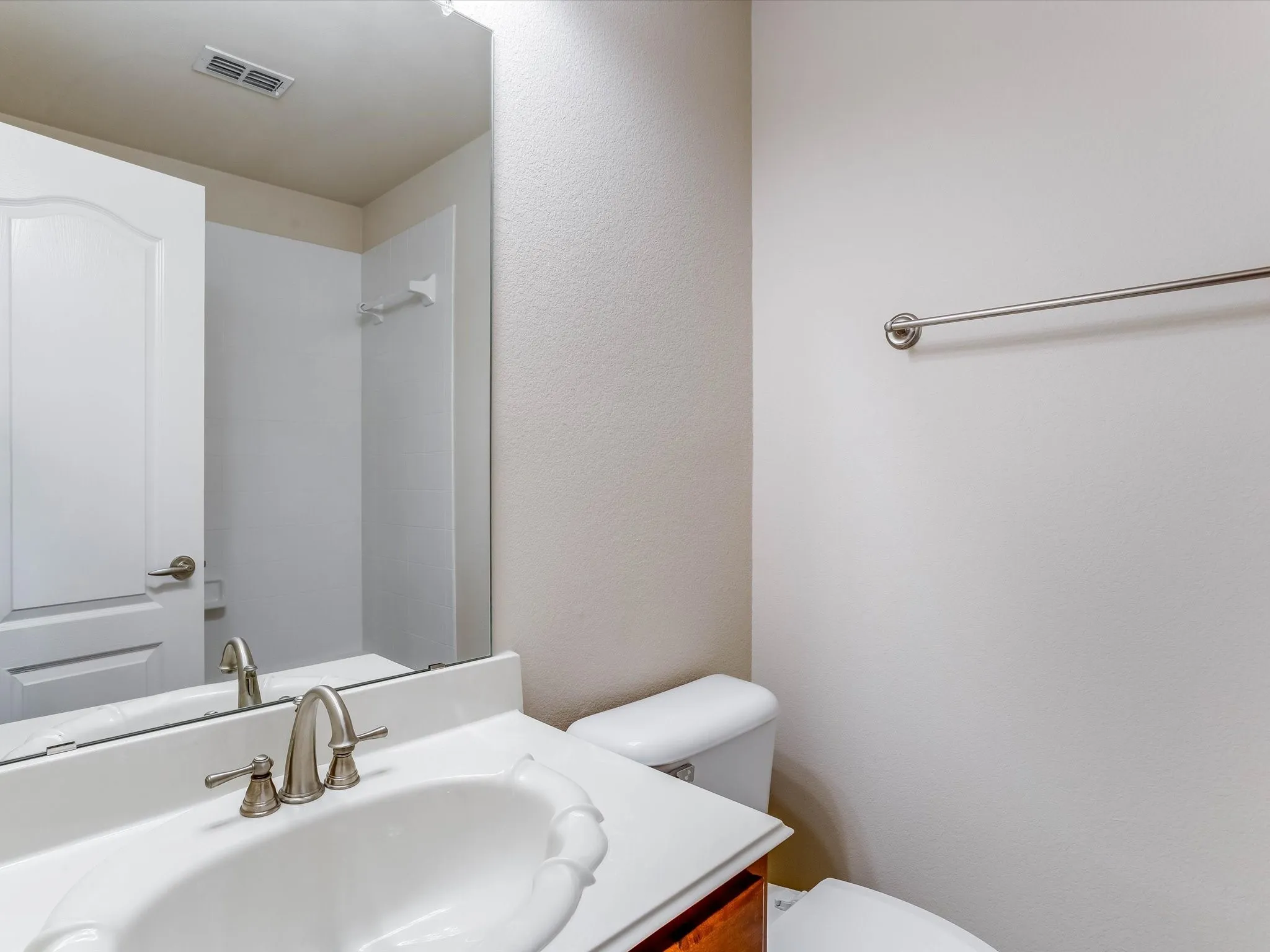 Bathroom featuring a vanity with a white integrated sink and countertop, polished chrome widespread faucet, expansive wall-mounted mirror, and a matching metal towel bar