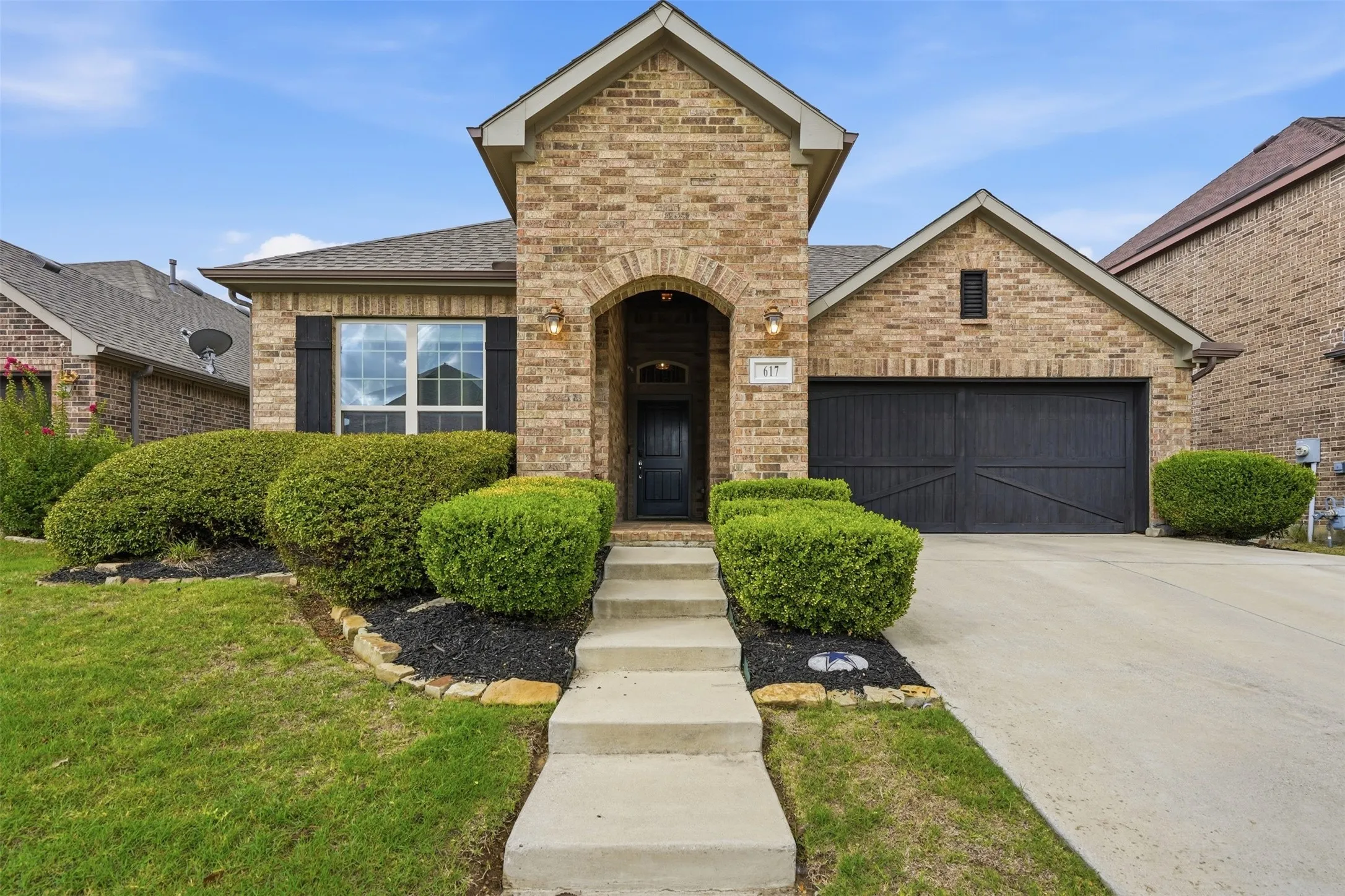 Brick exterior with a stone-accented arched entryway, dual-pane windows with dark shutters, and a two-car garage.