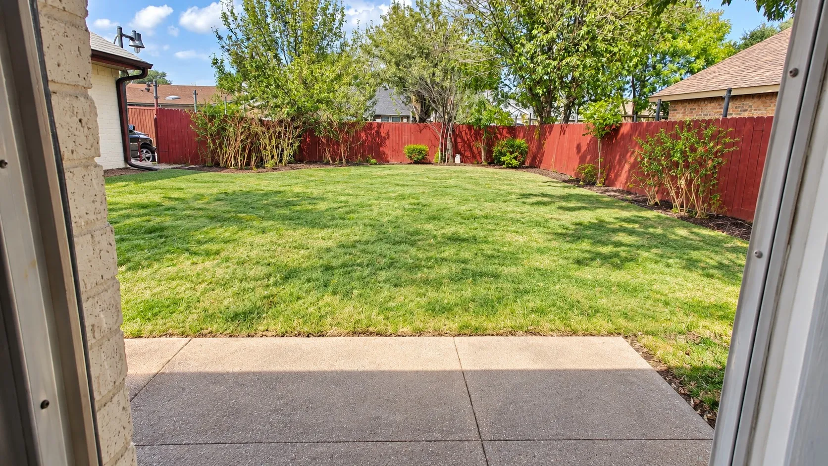 Backyard featuring a concrete patio, manicured lawn, and perimeter wood fencing