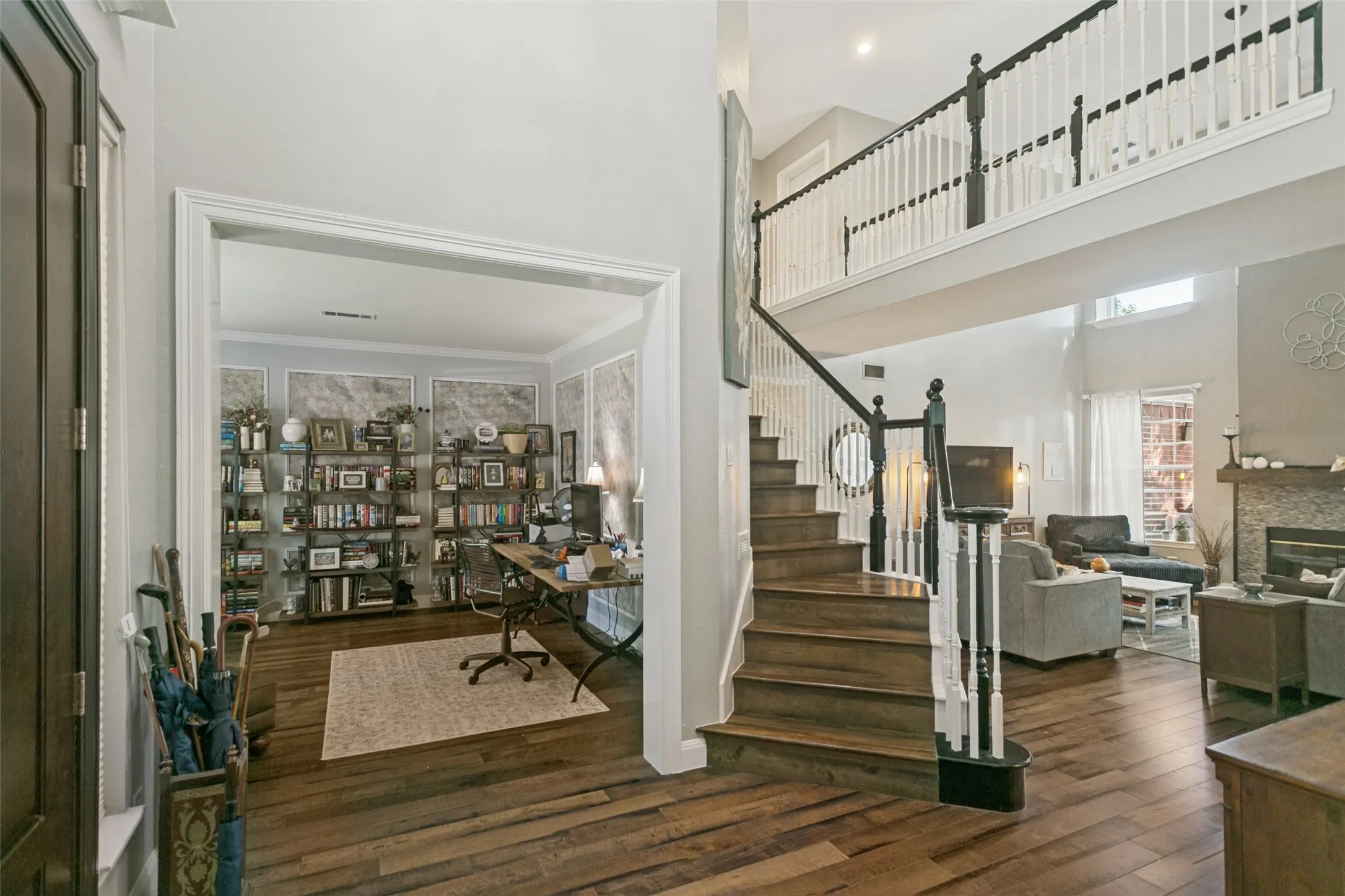 Two-story foyer featuring high ceilings, wood-finish flooring, a wood-tread staircase with white railings, and a stone-surround fireplace