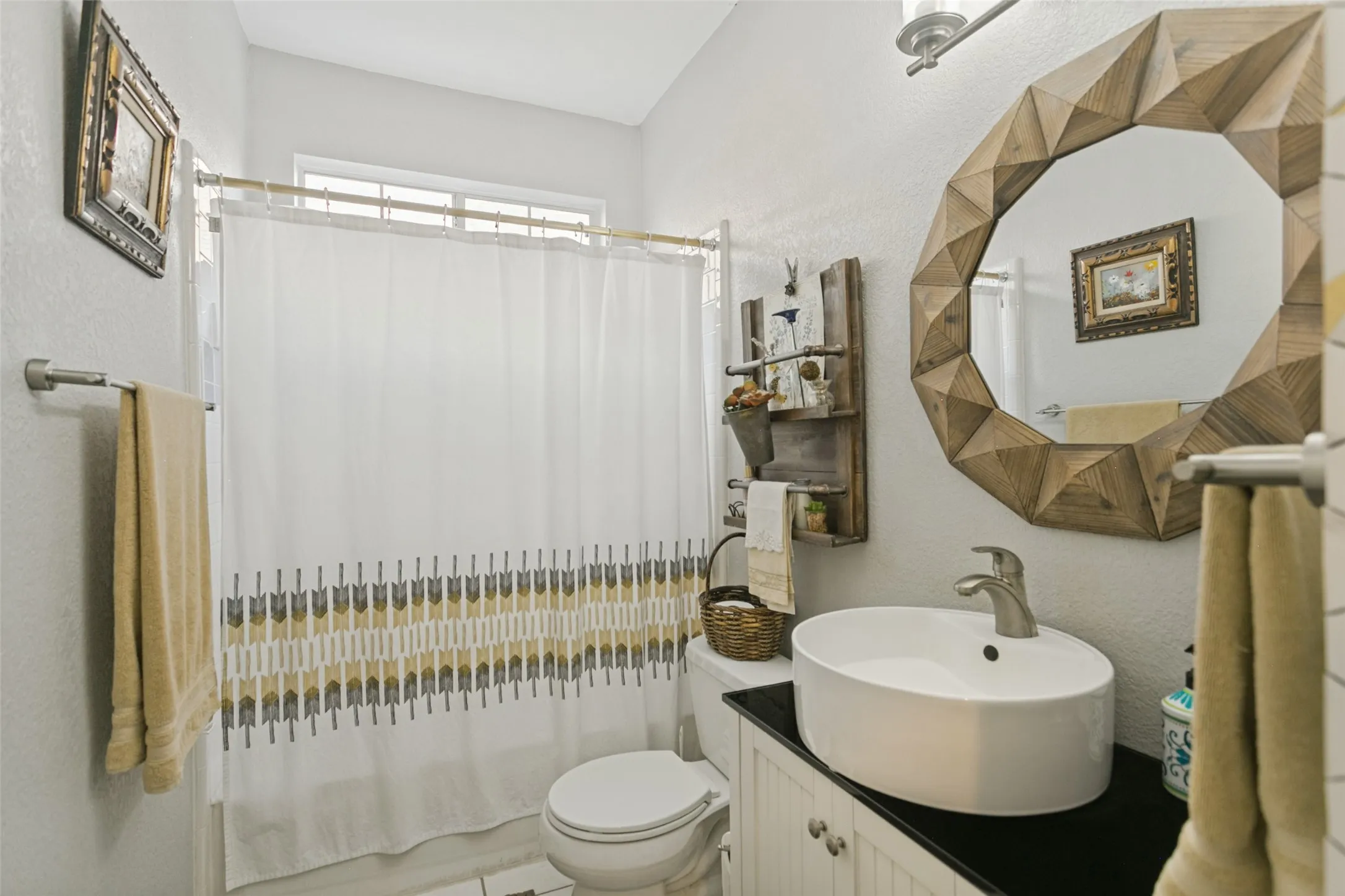 White oval vessel sink with a brushed-finish faucet, dark countertop, white beadboard vanity cabinet, and brushed-finish wall-mounted light fixture
