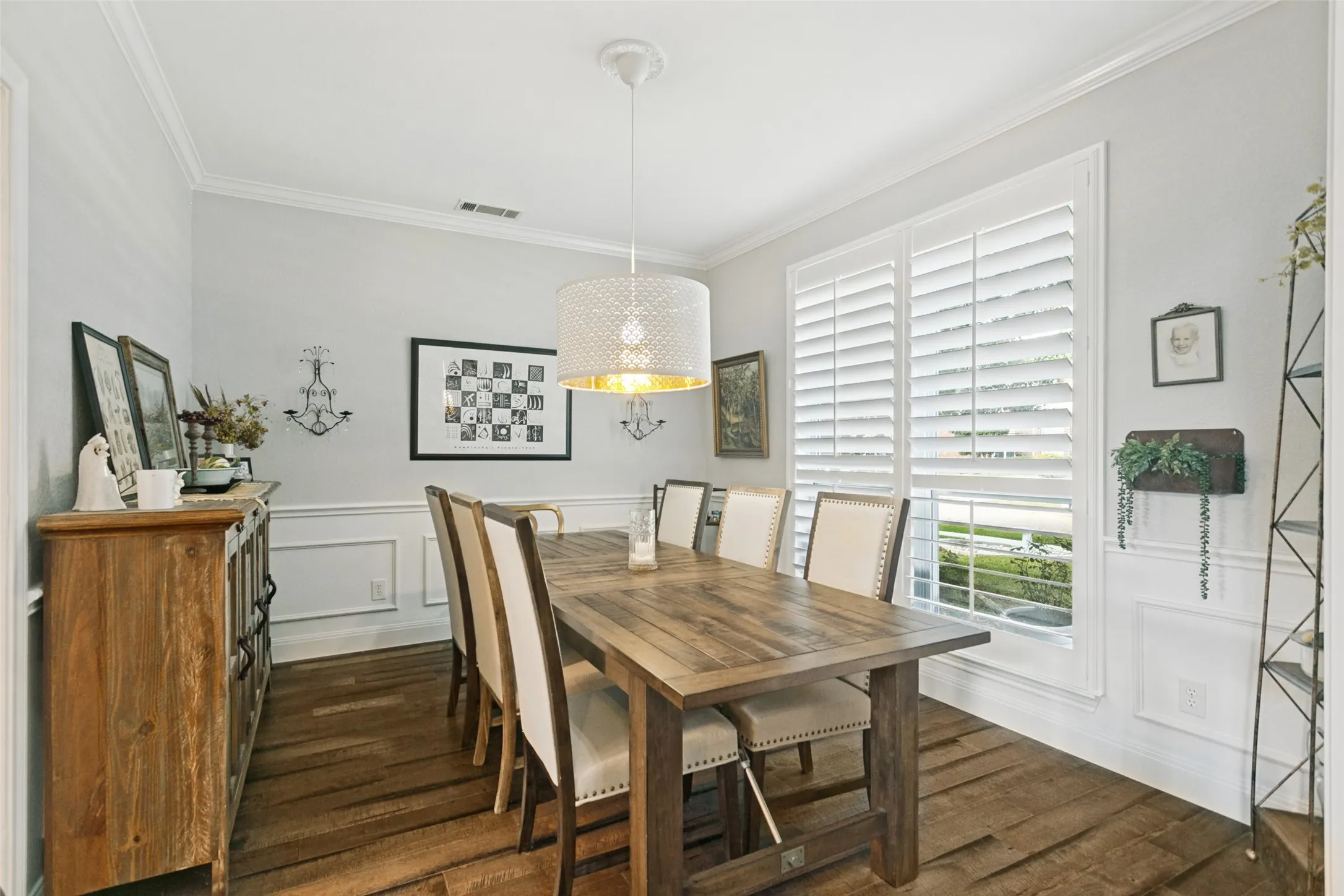Dining area featuring wood-finish flooring, wainscoting, crown molding, plantation shutters, and a drum pendant light fixture