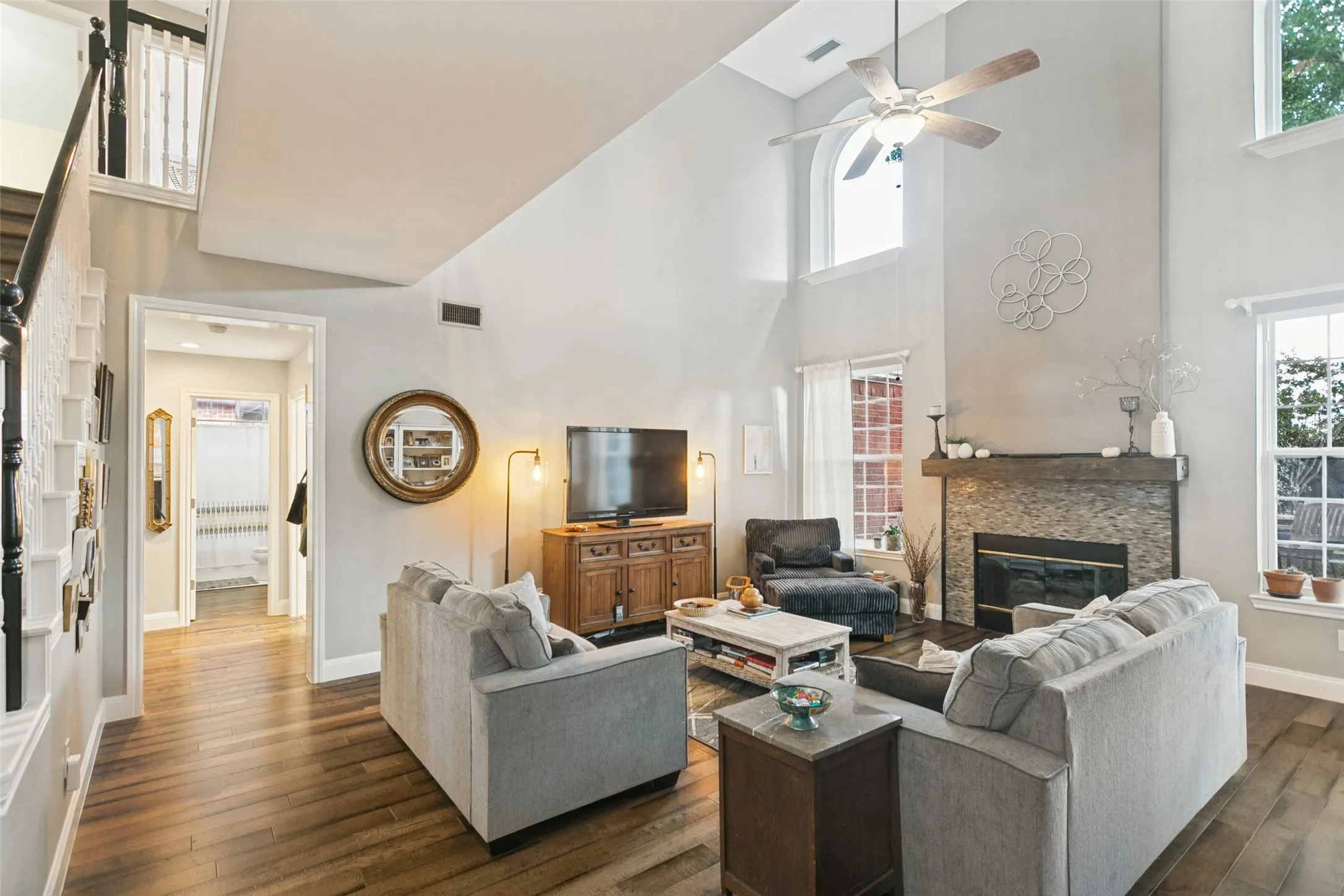 Living area featuring tall ceilings, a floor-to-ceiling fireplace with stone tile surround, wood-finish flooring, and arched windows