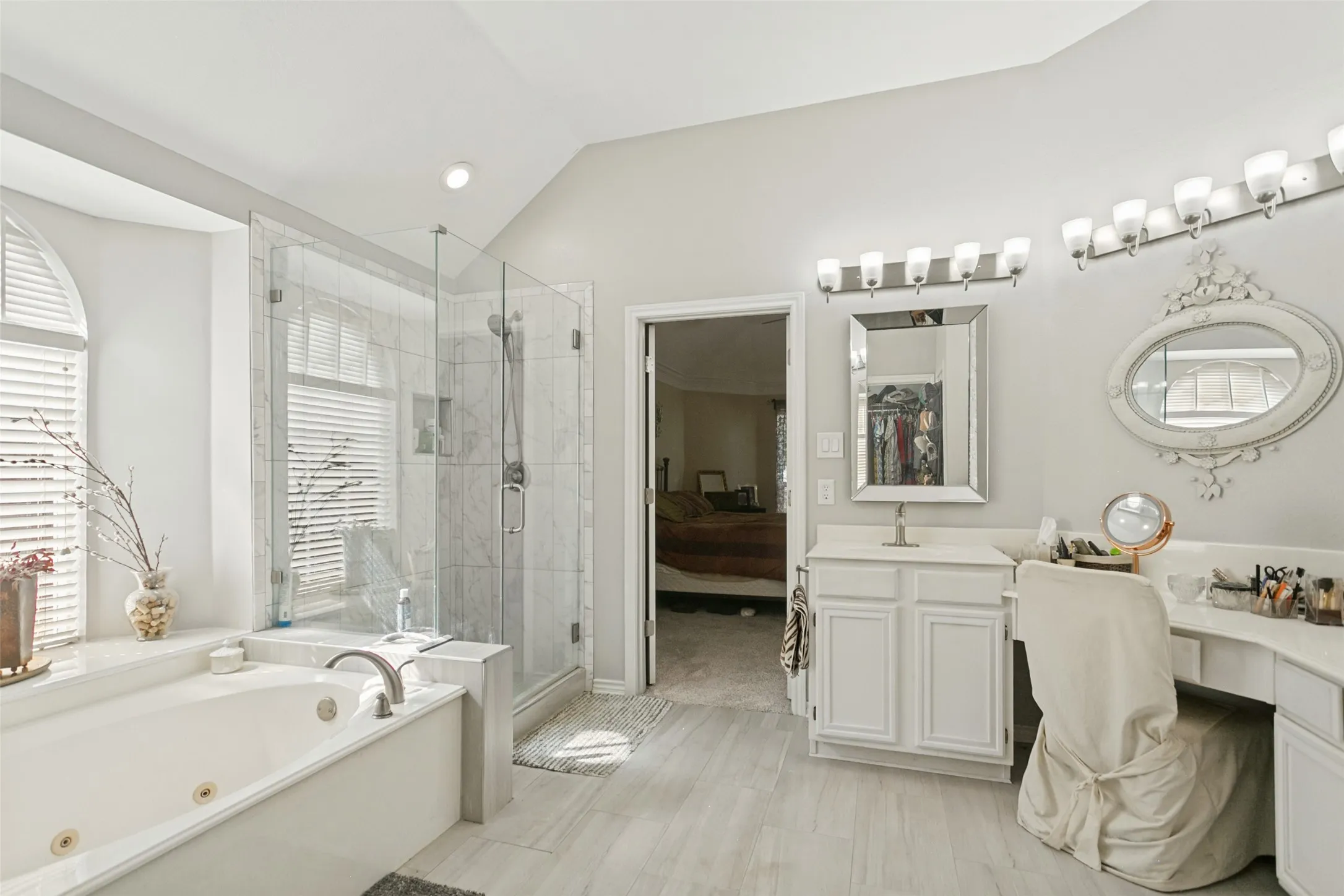 Bathroom featuring a jetted soaking tub, glass-enclosed shower with tiled surround, dual-mirrored vanity area with built-in cabinetry, and wood-finish flooring