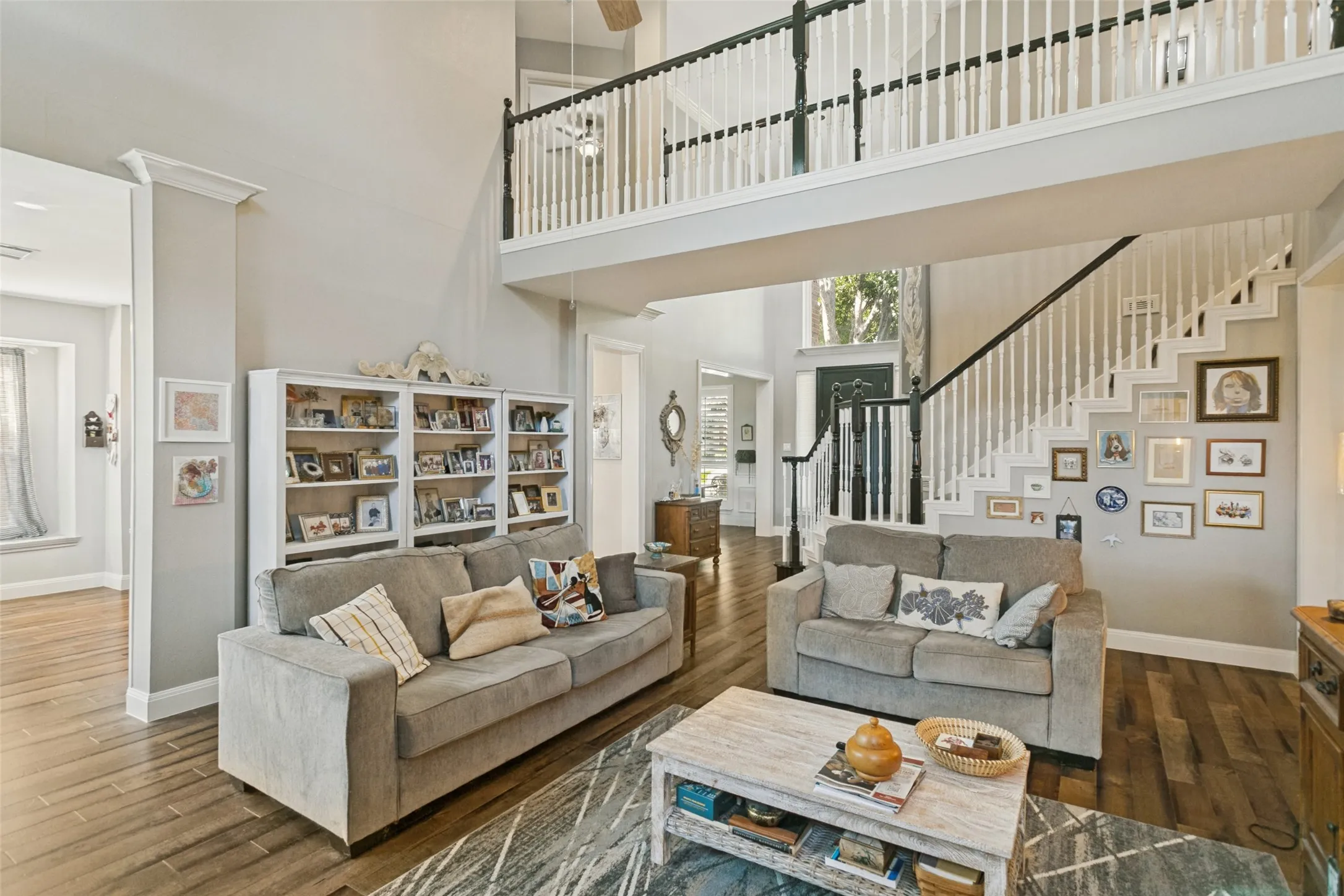 Two-story interior featuring tall ceilings, wood-finish flooring, a grand staircase with a painted wood balustrade, and built-in shelving