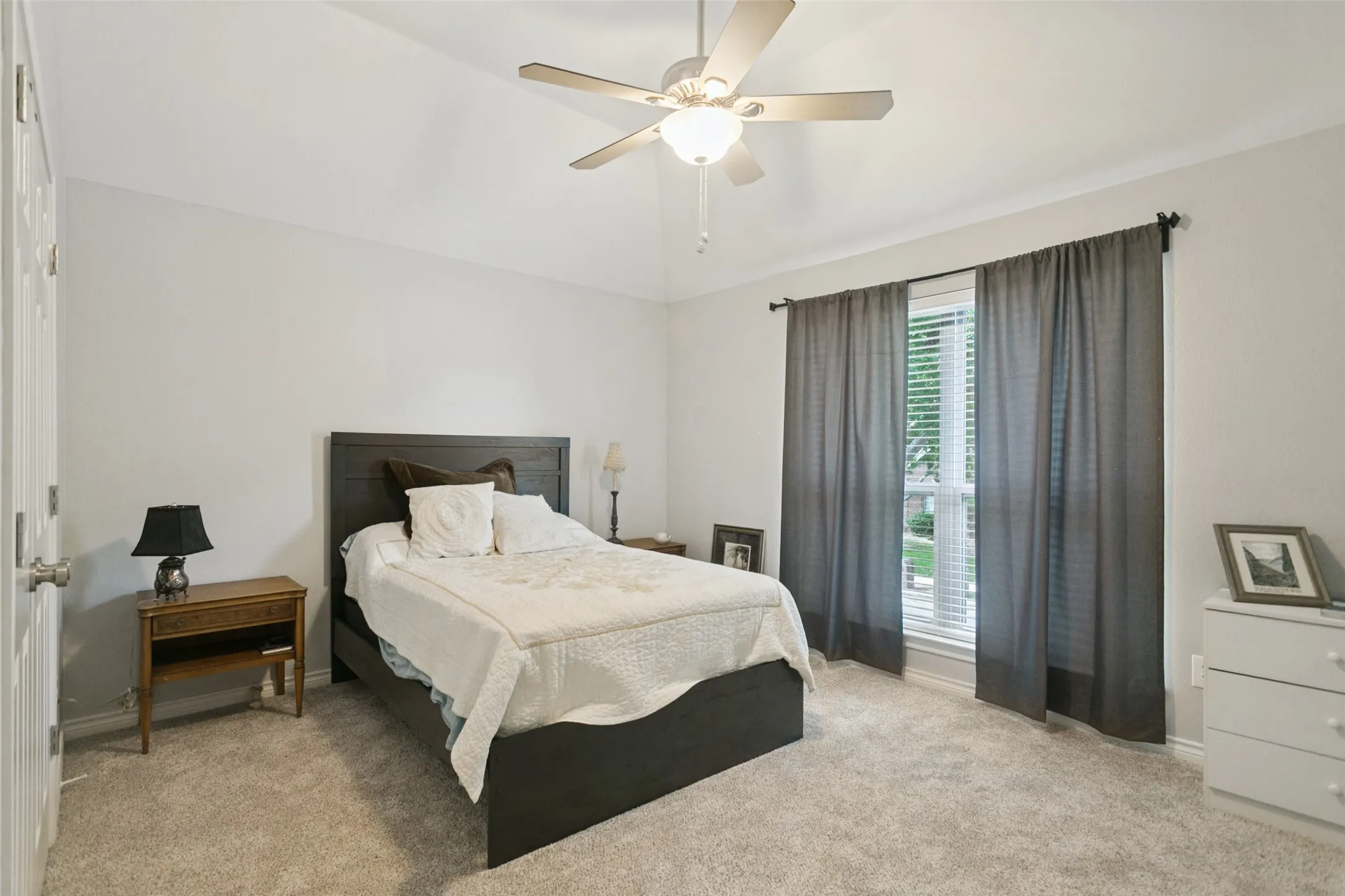 Vaulted ceiling, neutral wall tones, neutral carpeting, and a multi-blade ceiling fan with integrated lighting