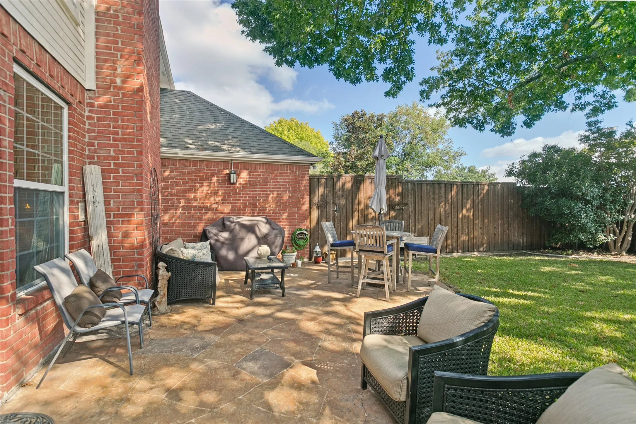 Flagstone patio featuring a red brick exterior wall, solid wood fencing, and mature trees