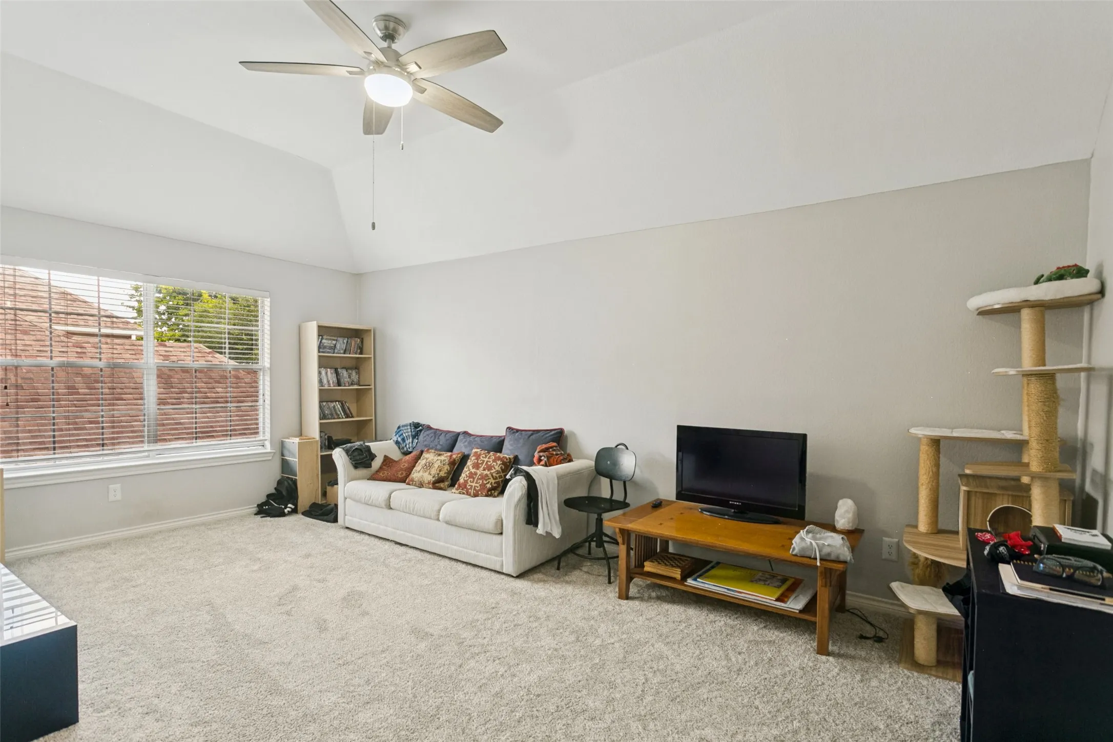 Vaulted ceilings, neutral wall tones, wall-to-wall carpeting, and a multi-blade ceiling fan with integrated lighting