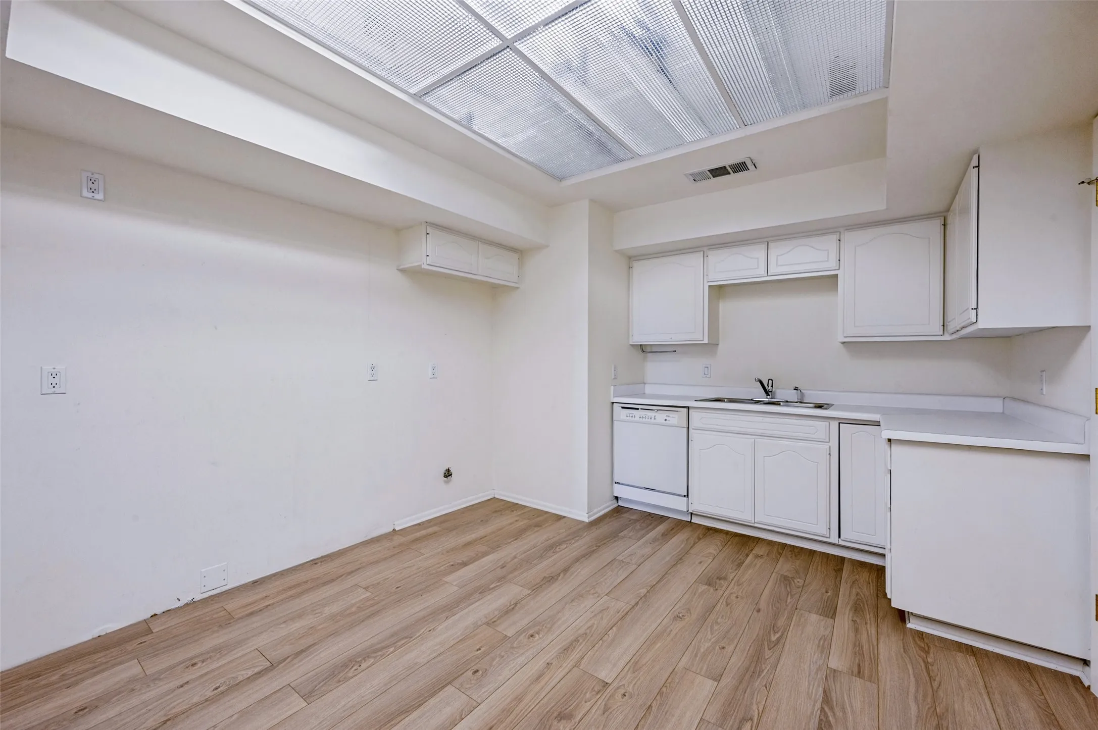 Kitchen featuring white cabinetry, wood-finish flooring, a stainless steel sink with a high-arch faucet, a built-in dishwasher, and a recessed ceiling light panel