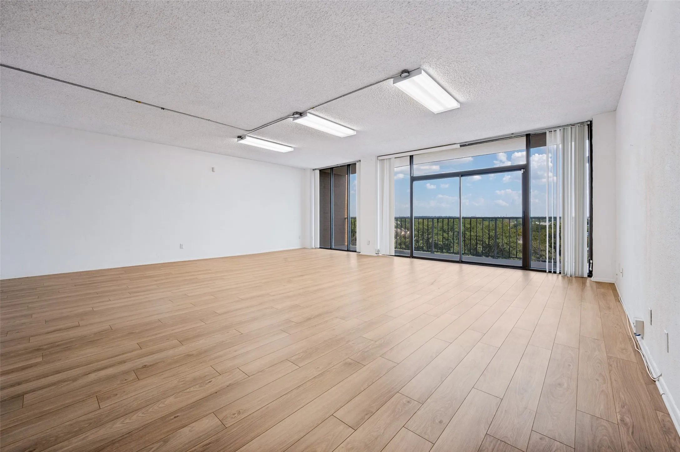 Expansive living area featuring wood-finish flooring, sliding glass doors, floor-to-ceiling windows, and linear track lighting